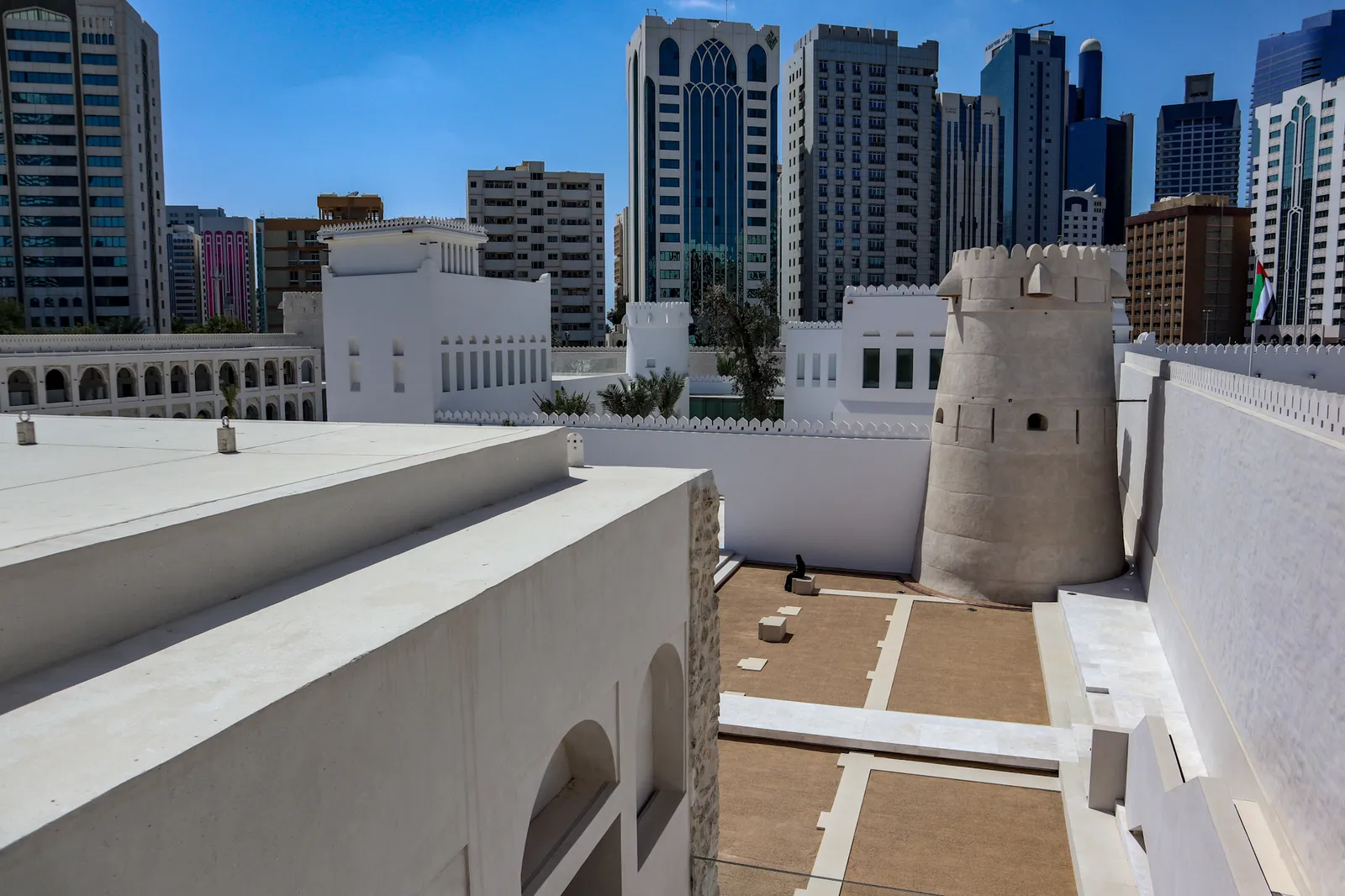The round coral-stone watchtower and whitewashed walls of Qasr Al Hosn in Abu Dhabi, with the glass and concrete towers of the modern city rising directly behind it