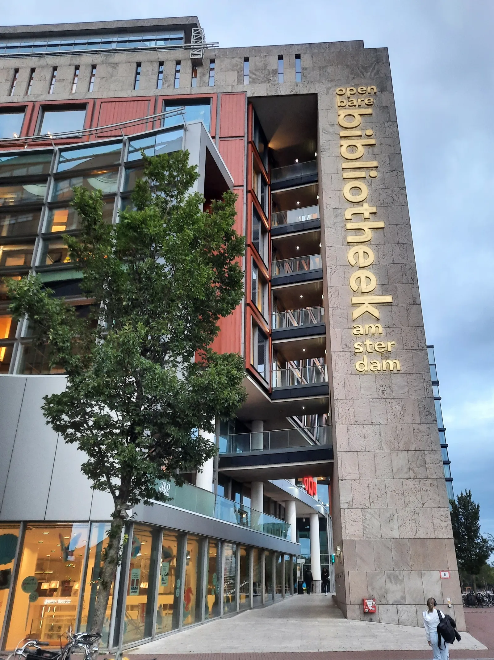 The Openbare Bibliotheek Amsterdam (OBA) central library building at Oosterdok, its stacked glass and stone facade rising above the street with the library's name lettered vertically down one tower