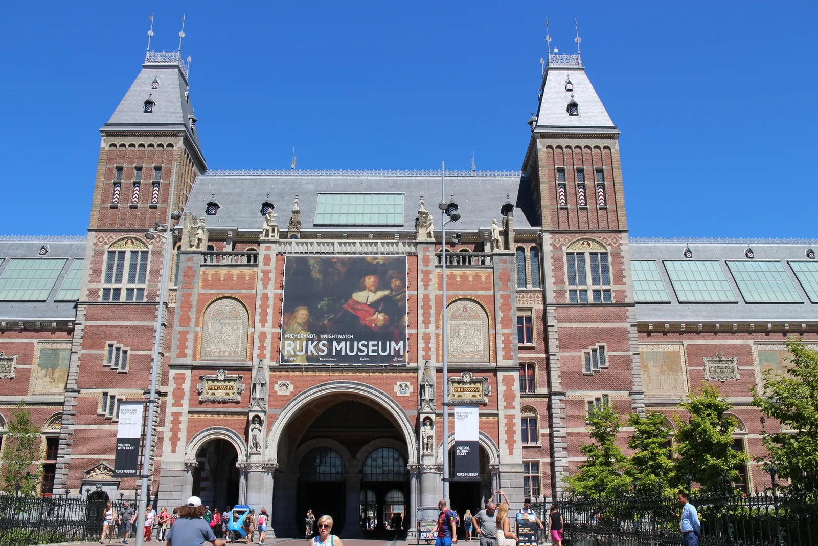 The south facade of the Rijksmuseum in Amsterdam seen from Museumplein, its twin brick towers flanking the central archway that cuts through the building