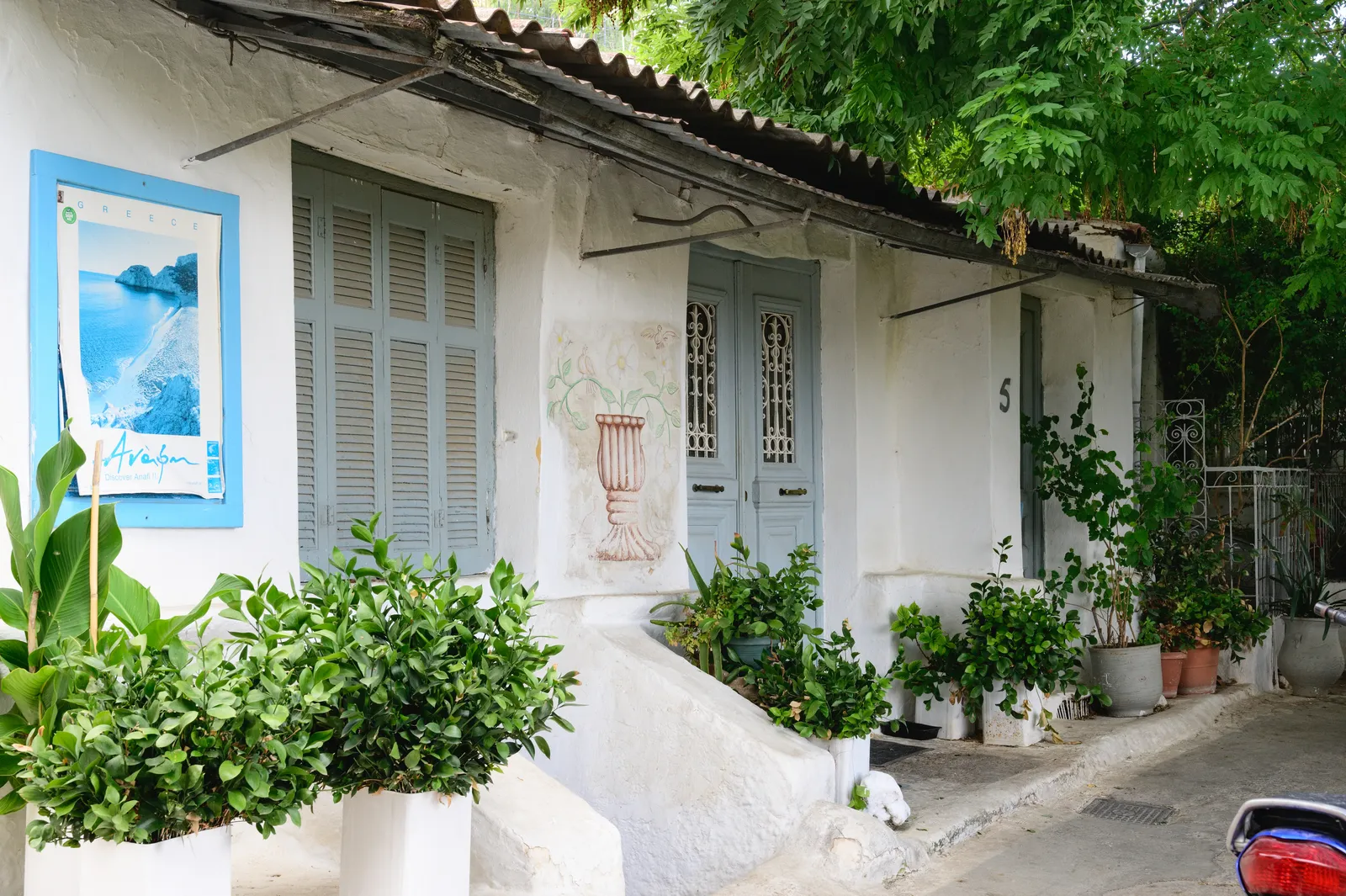 A whitewashed cottage in Anafiotika, Athens, with pale blue shutters and doors and potted plants lining the step in front of it