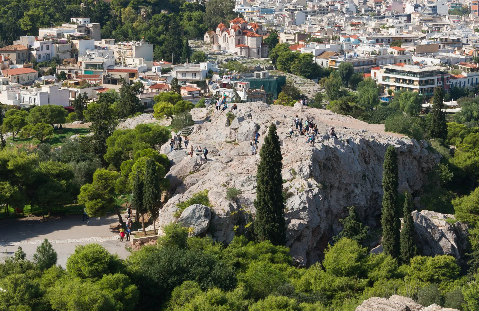 The bare limestone dome of the Areopagus rock in Athens with visitors standing on top of it and the city spreading out behind