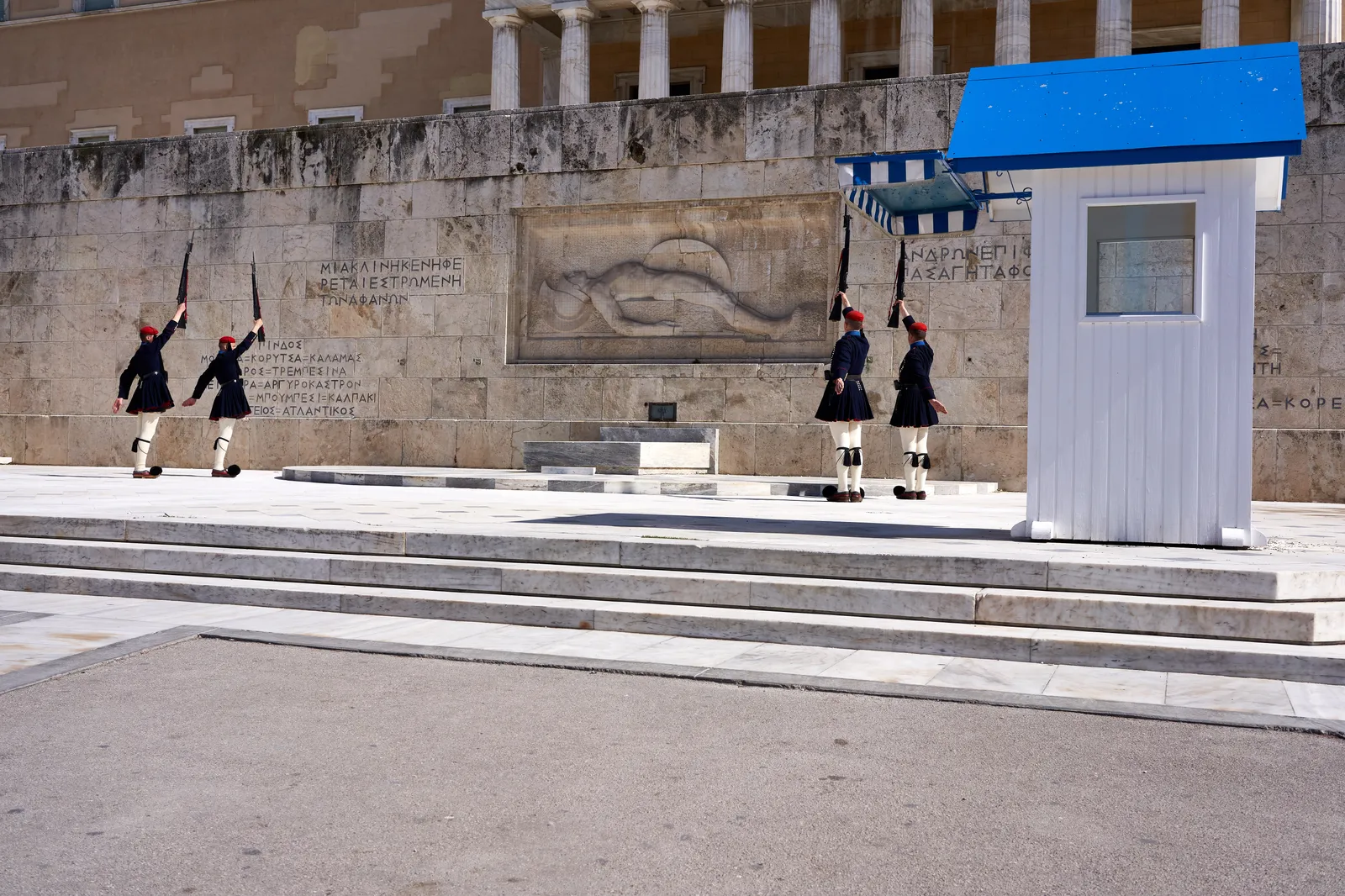 Four Evzones of the Greek Presidential Guard in pleated kilts and pom-pom shoes mid-ceremony at the Tomb of the Unknown Soldier in Athens