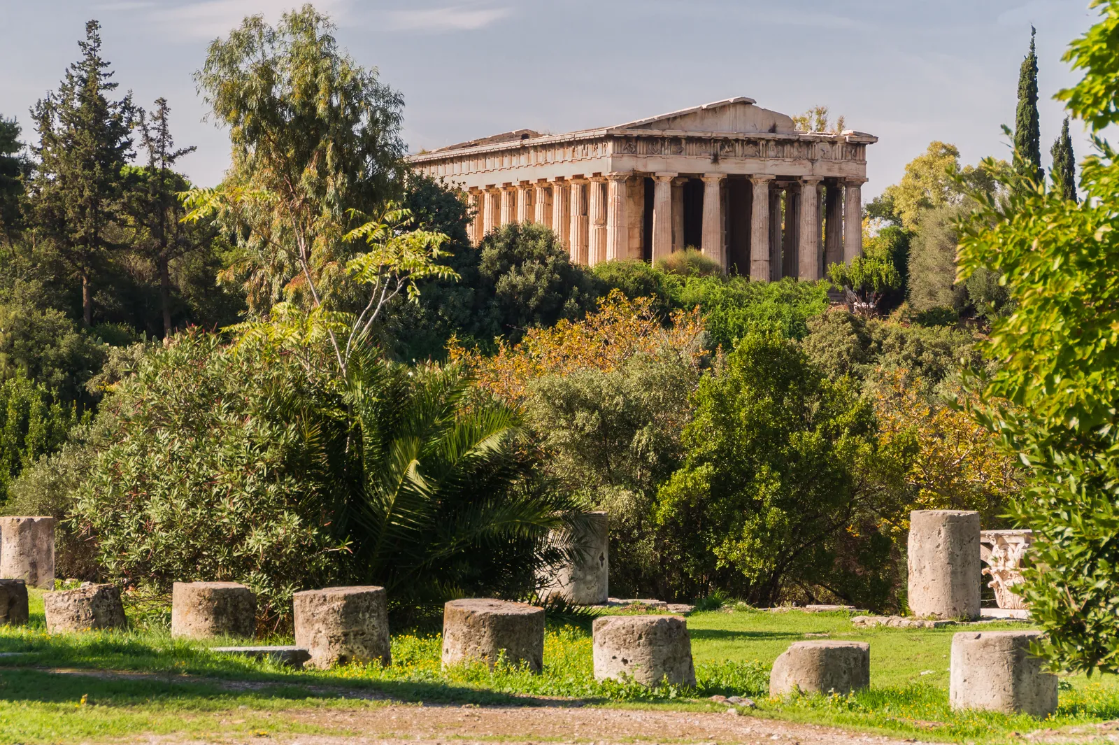 The Temple of Hephaestus in the Ancient Agora of Athens, its full colonnade standing above the trees, with cut column drums lying in the grass in the foreground