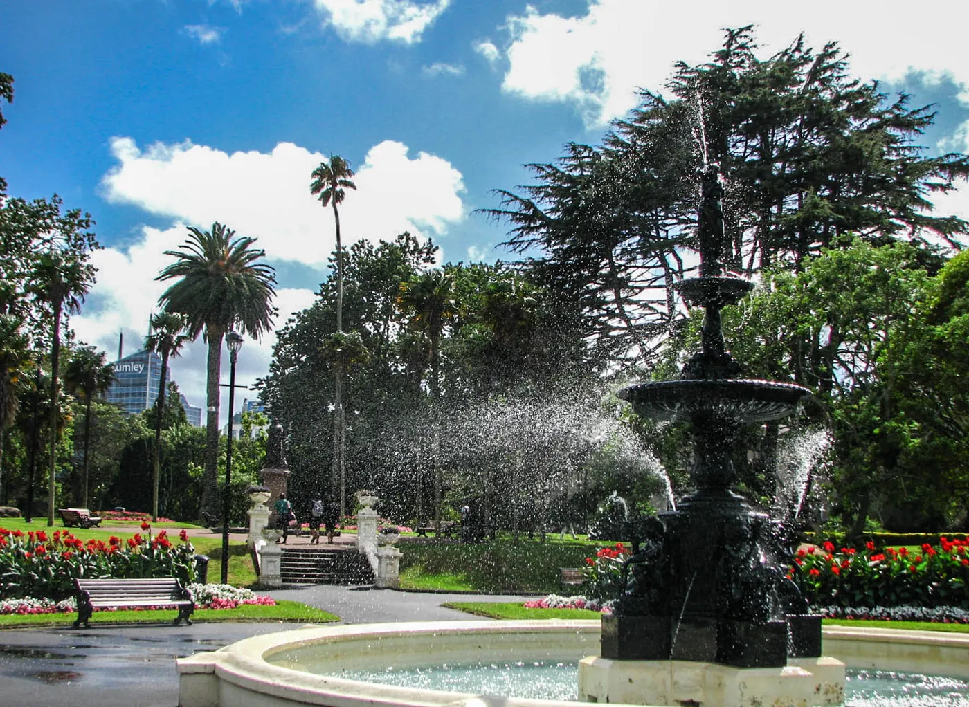 The cast-iron fountain at the top of Albert Park in Auckland throwing spray across its basin, with flowerbeds, palms and tall trees around it