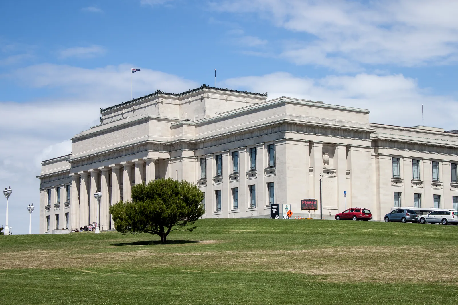 Auckland War Memorial Museum, a pale stone building with a columned portico, standing above a wide sloping lawn in the Auckland Domain