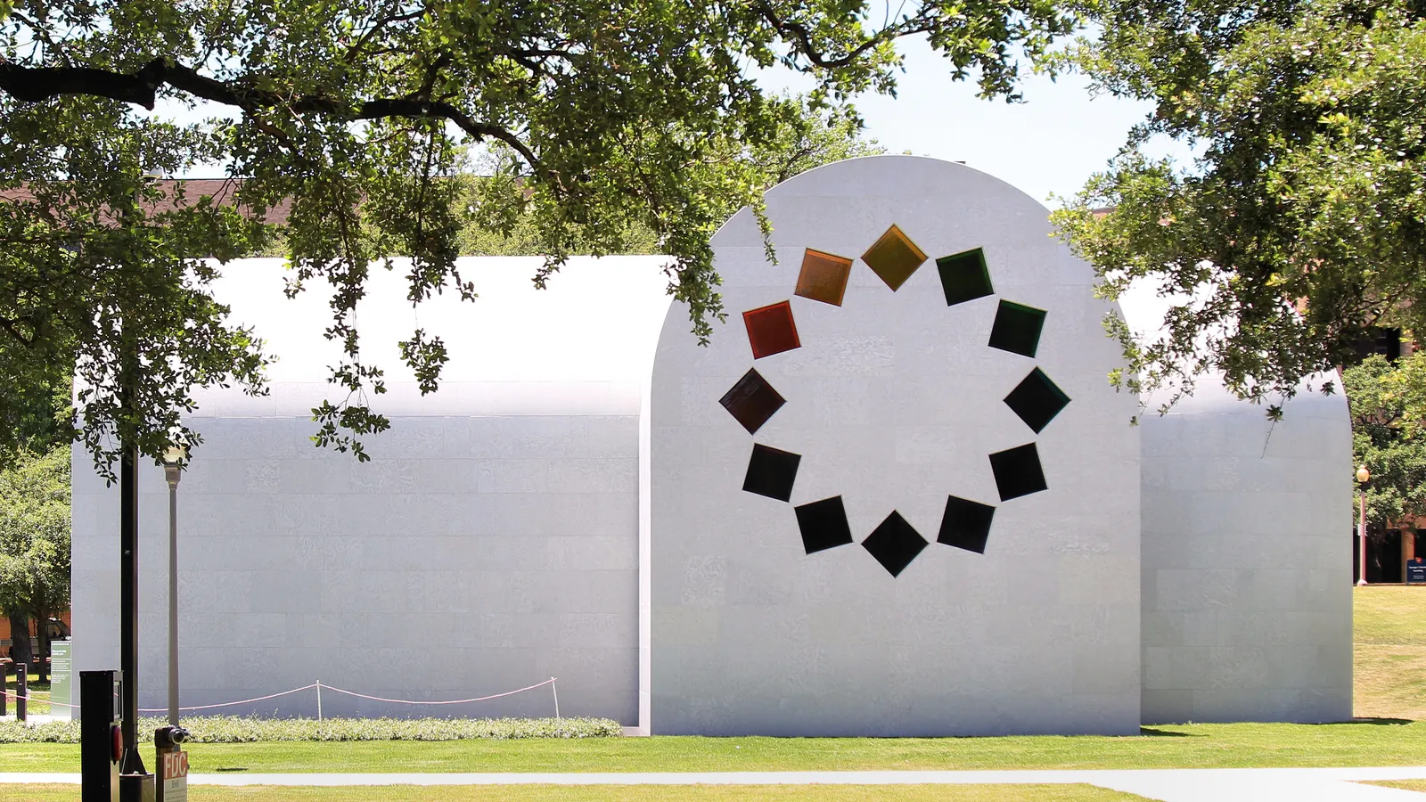 Ellsworth Kelly's building at the Blanton Museum of Art in Austin, a small white stone structure with rounded barrel vaults and a ring of colored glass diamonds set into the end wall, framed by live oak branches