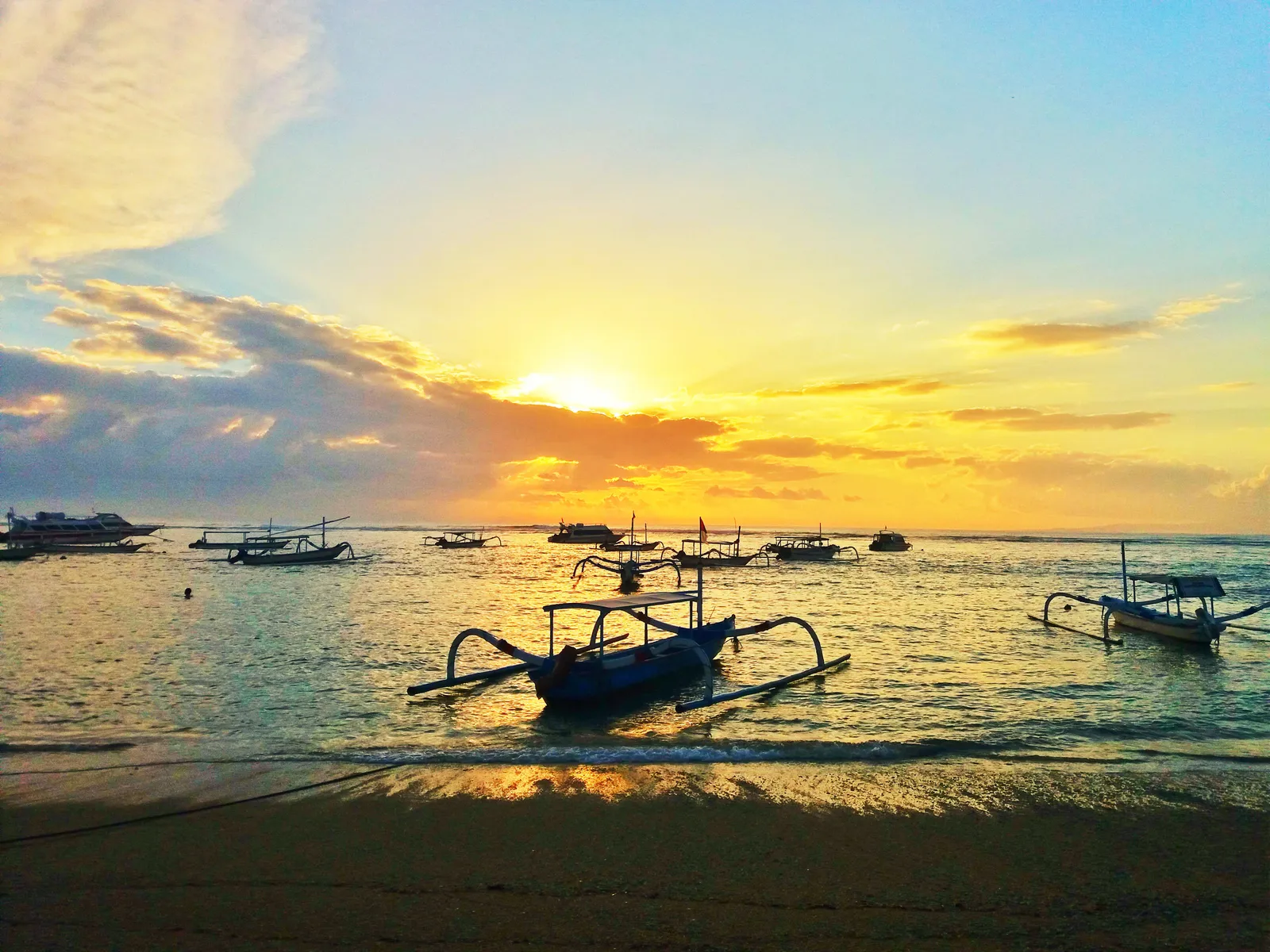 Sunrise over the sea at Sanur in Bali, with outrigger fishing boats drawn up on the wet sand in the foreground