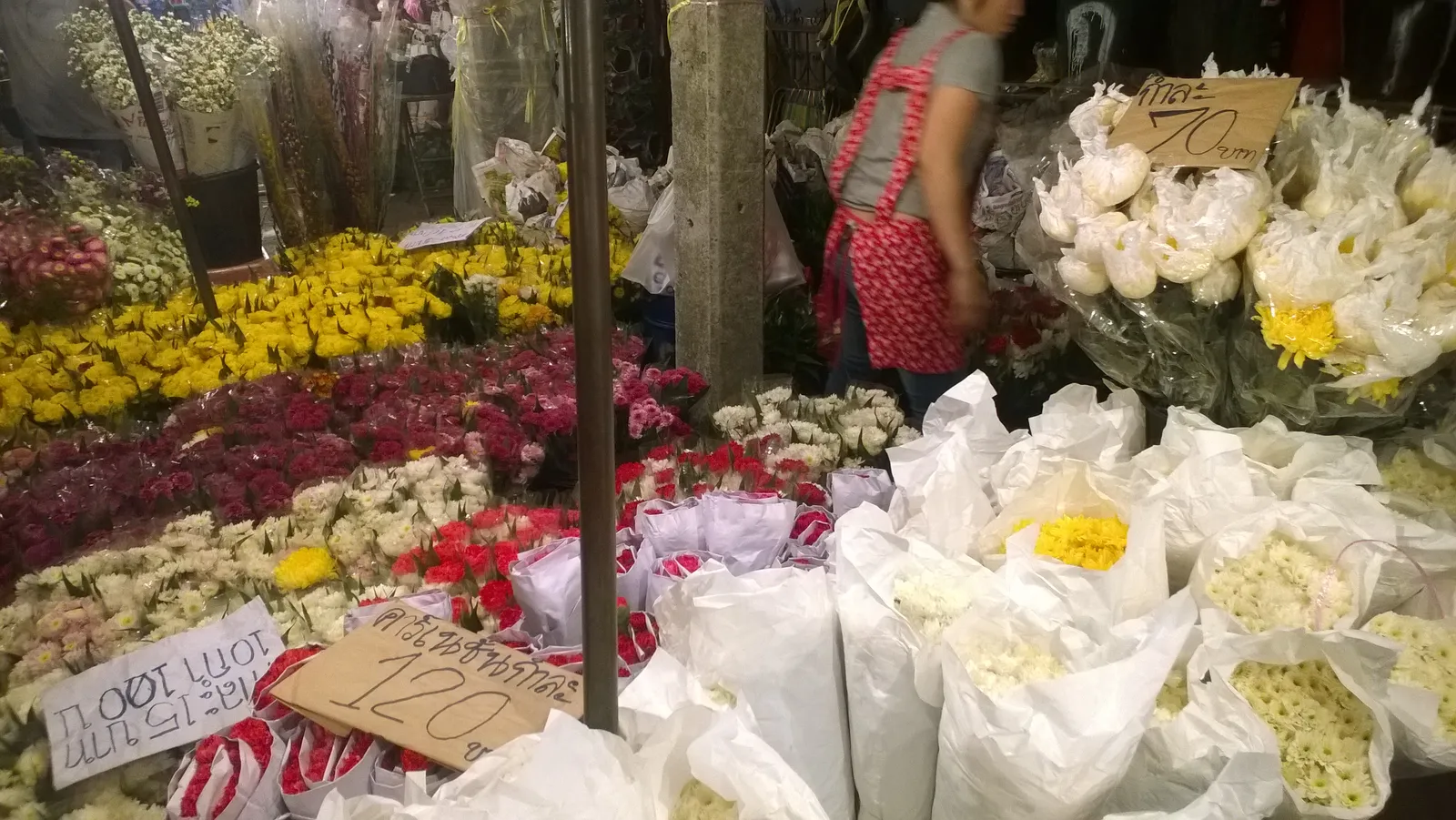 Stalls at Pak Khlong Talat flower market in Bangkok banked with yellow marigolds, pink and white roses and bagged jasmine buds, handwritten baht price cards propped among them