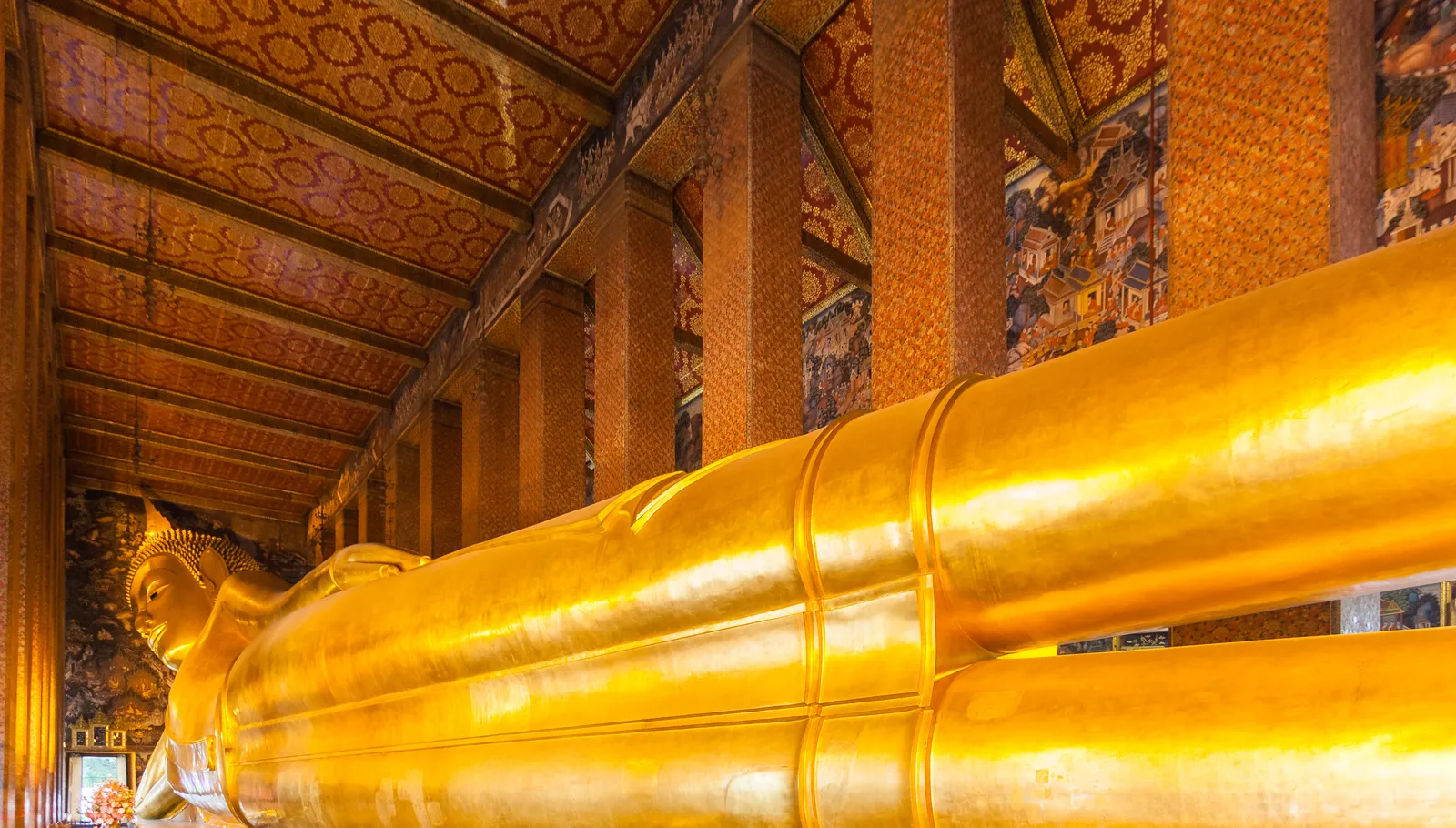 The gilded reclining Buddha at Wat Pho in Bangkok filling the length of its hall, the figure's head resting on a stack of cushions at the far end and gold columns running down the wall beside it