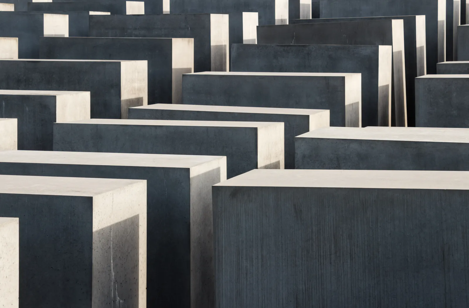 Rows of grey concrete stelae of varying heights at the Memorial to the Murdered Jews of Europe in Berlin, receding across the sloping ground in strong sunlight
