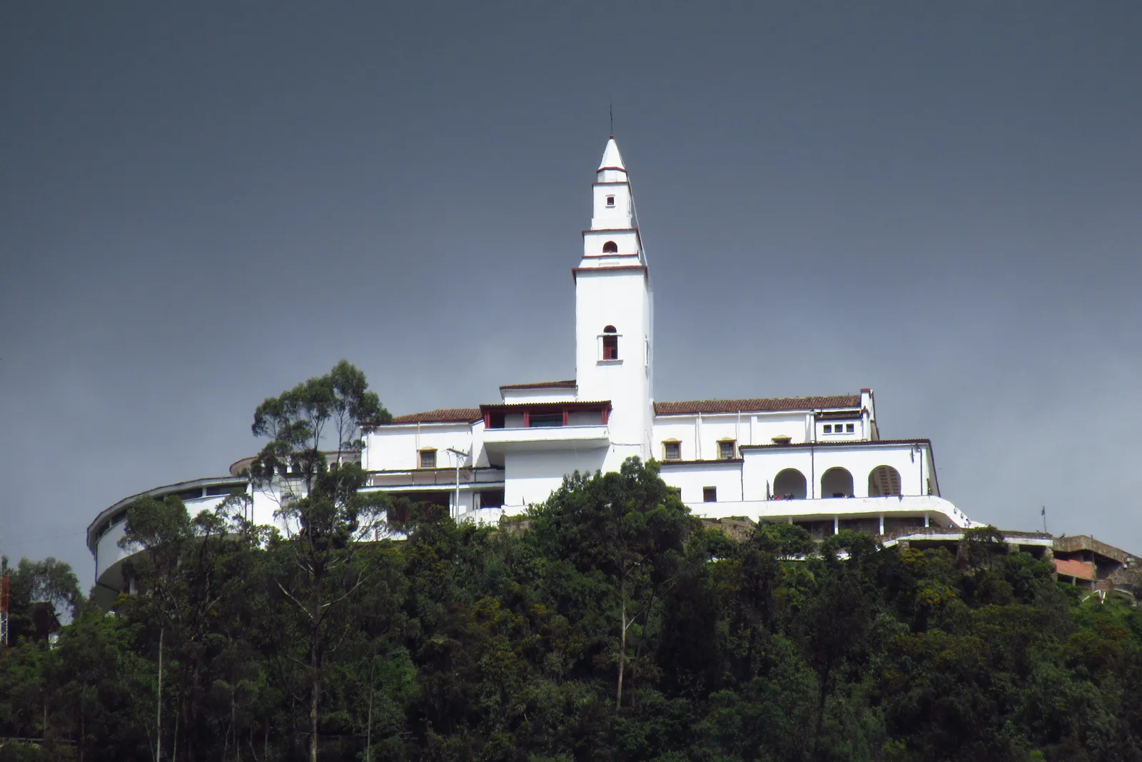 The white sanctuary church on the summit of Monserrate above Bogotá, its single bell tower rising over a long low white building surrounded by forest