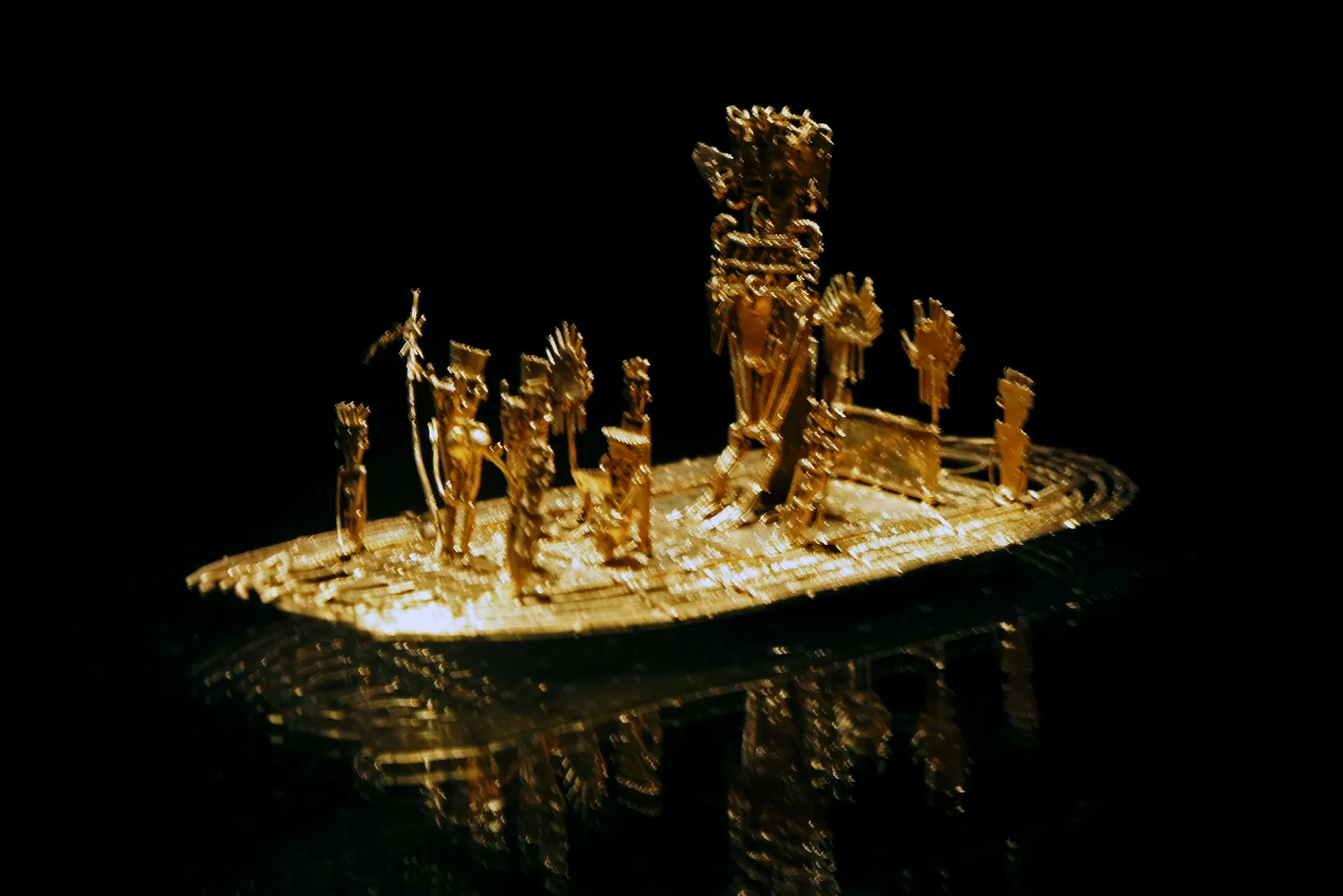 The Muisca raft in Bogotá's Museo del Oro, a small gold raft carrying a central figure surrounded by attendants, lit against a black background