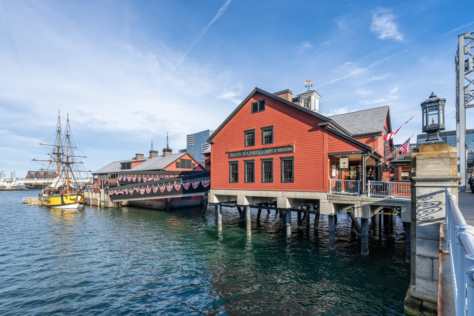 The red clapboard Boston Tea Party Ships and Museum standing on pilings over Fort Point Channel, with a replica square-rigged brig moored alongside it