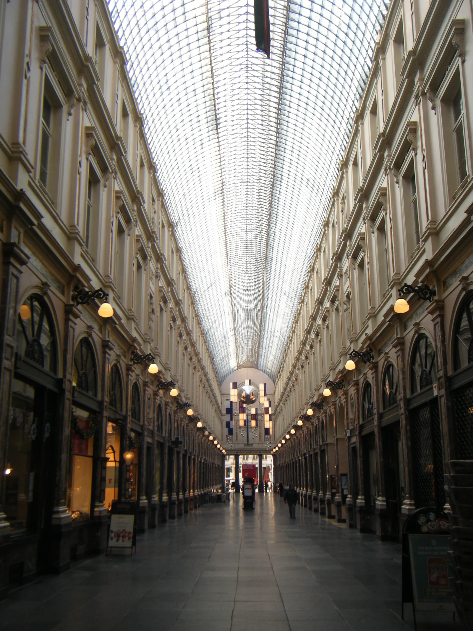 The interior of the Galeries Royales Saint-Hubert in Brussels, shopfronts and lamps running the length of the arcade beneath a long barrel roof of iron and glass