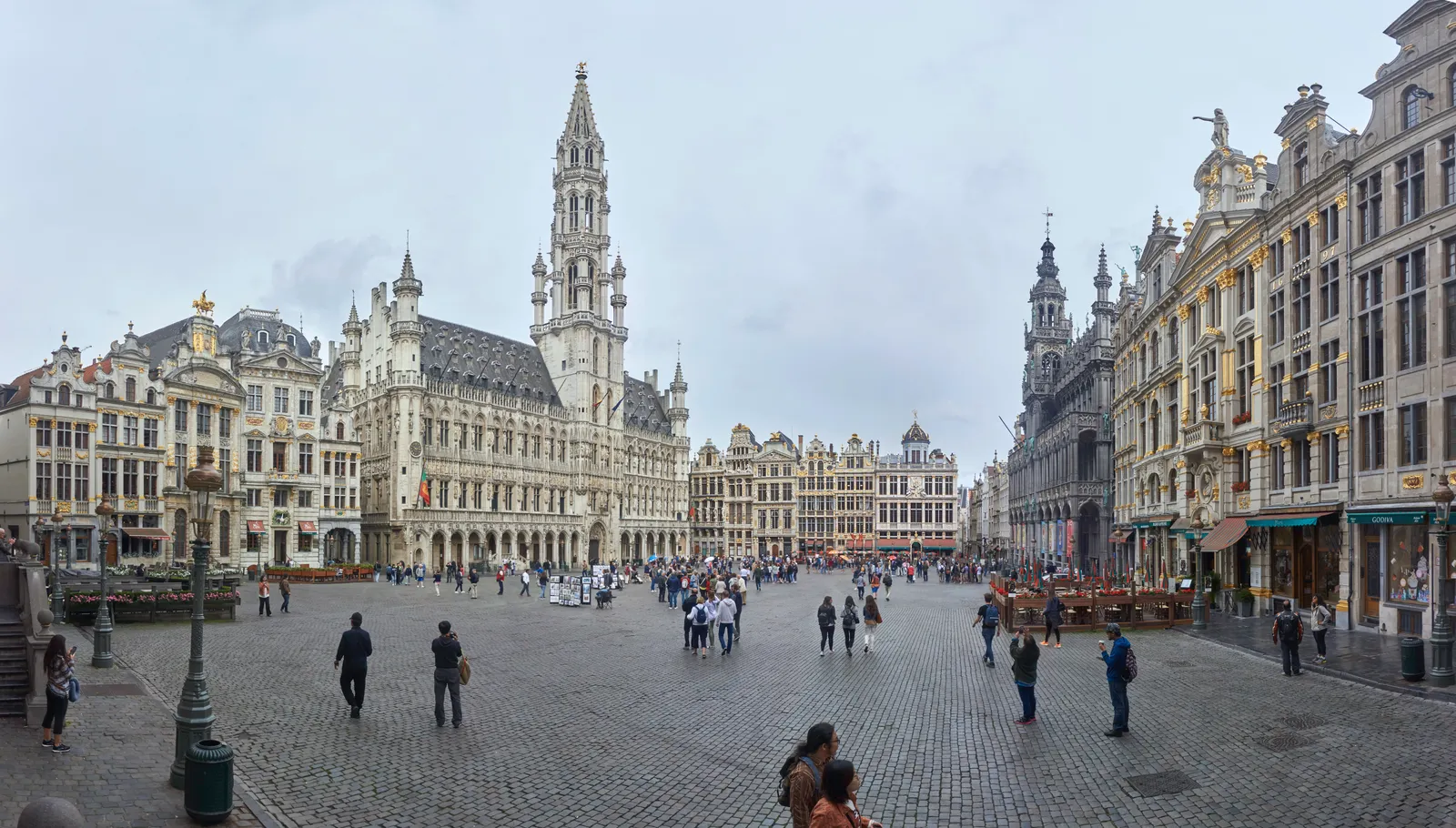 The Grand-Place in Brussels seen across its cobbles, gilded guildhall gables lining three sides of the square and the Town Hall's tall Gothic spire rising from the fourth