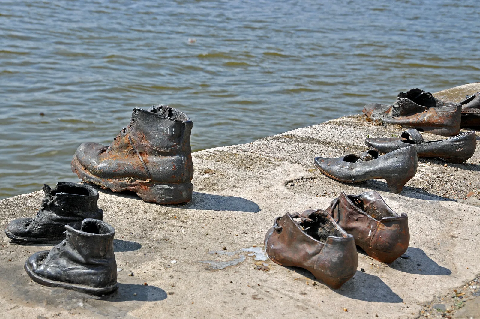 Cast-iron shoes of the Shoes on the Danube Bank memorial in Budapest, men's boots and smaller shoes left in a row on the stone quay at the edge of the river