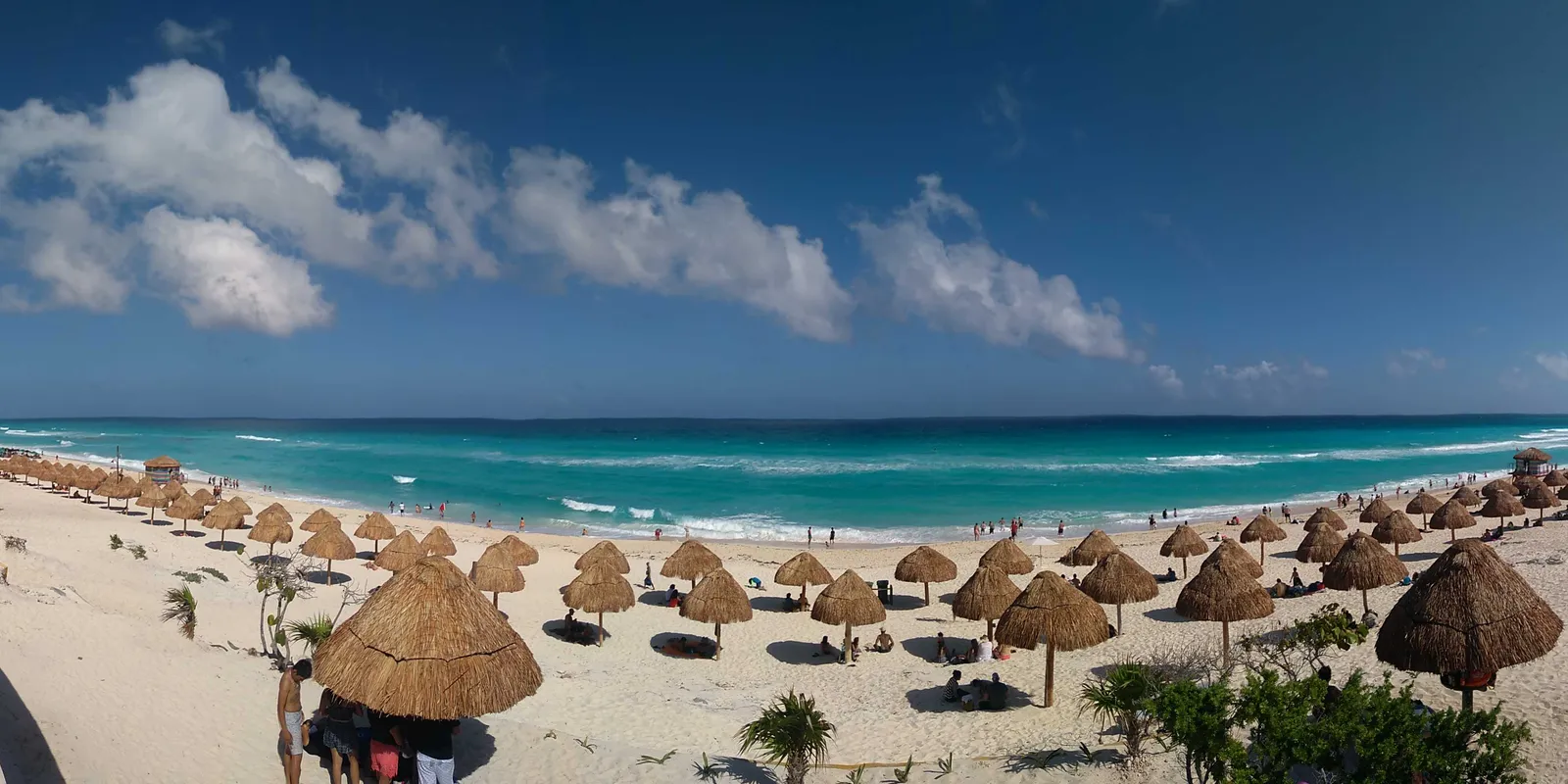 Playa Delfines in Cancún, rows of thatched umbrellas spread across wide white sand with turquoise Caribbean surf beyond and no buildings along the shore