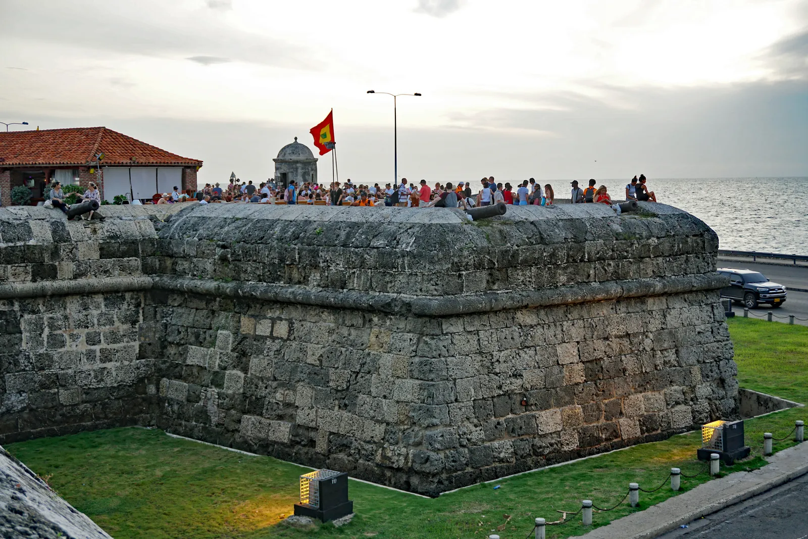 A crowd of people gathered on top of the stone Baluarte de Santo Domingo bastion in Cartagena at dusk, watching the sun set over the Caribbean Sea