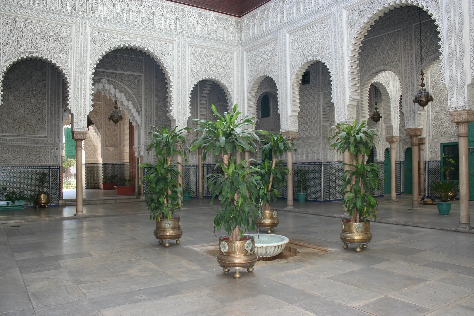The main hall of the Mahkama du Pacha in Casablanca, horseshoe arches on carved columns around a marble floor, white stucco fretwork covering the upper walls and zellige tilework along the base