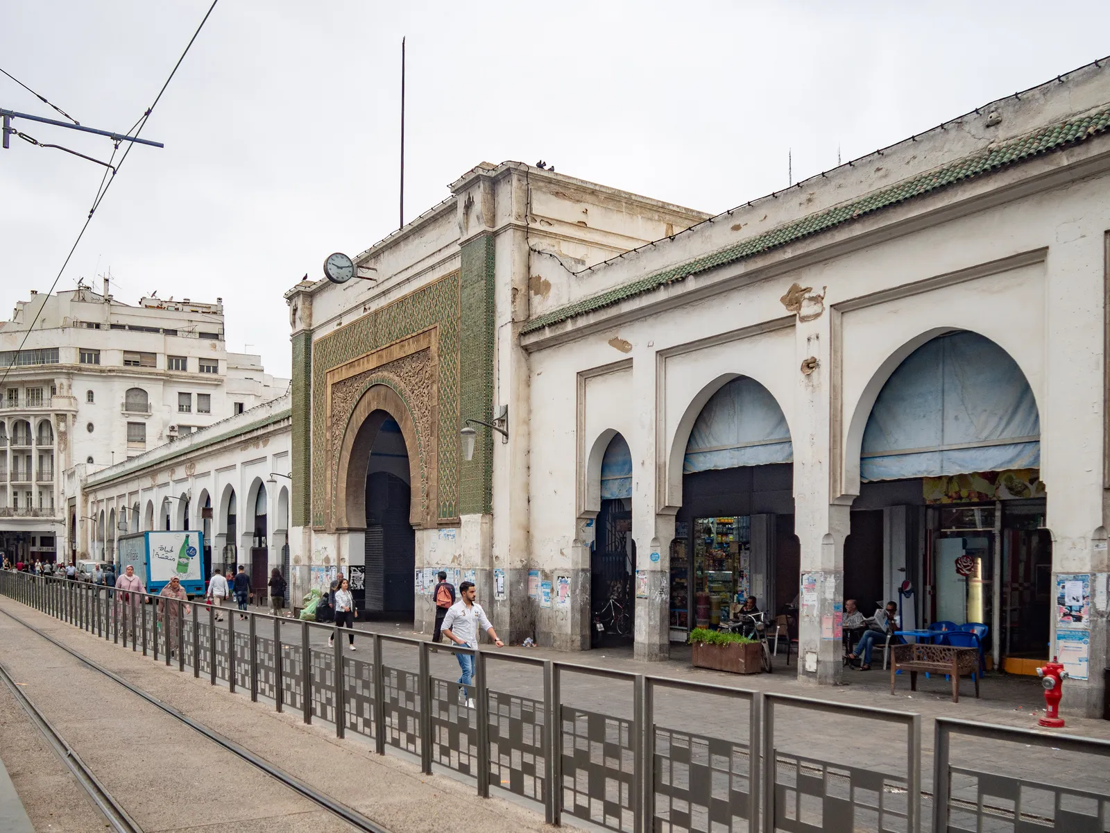 The long arcaded frontage of the Marché Central on Boulevard Mohammed V in Casablanca, its green tiled central gateway set into a white wall, with tram tracks running past in the foreground
