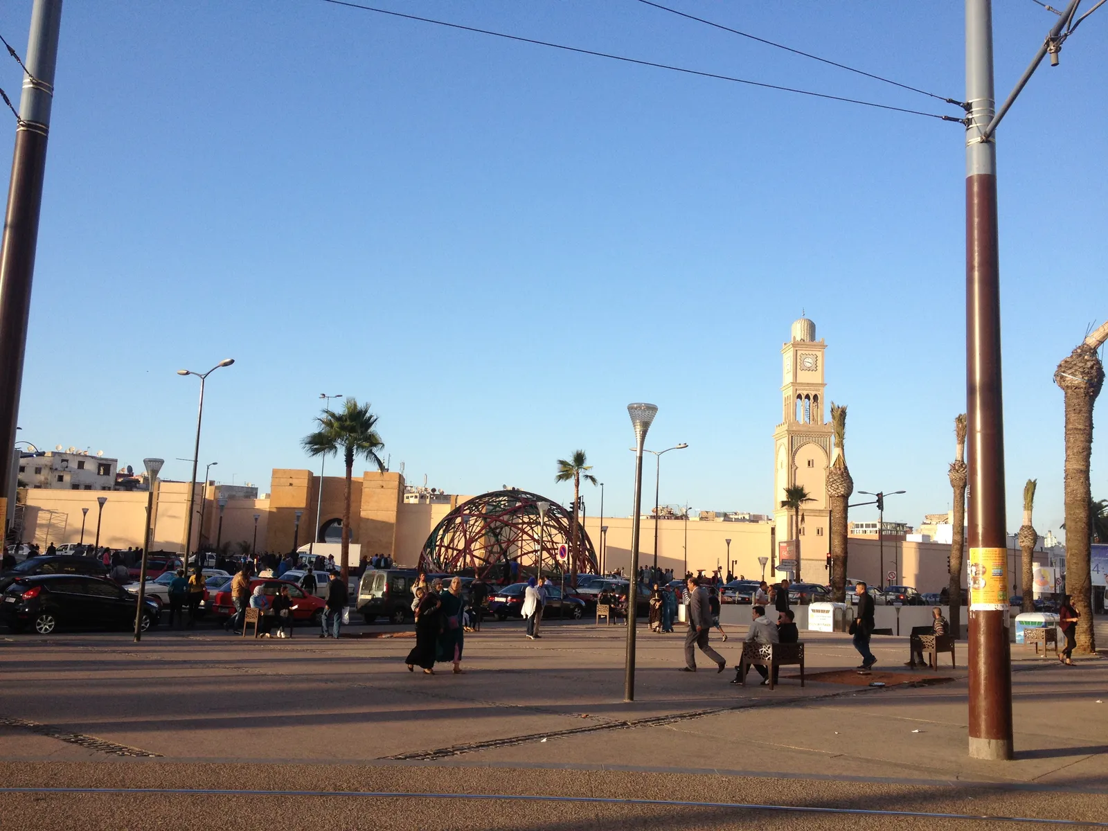 The sand-coloured outer wall of Casablanca's old medina seen from United Nations Square, with the white clock tower standing above the rooftops on the right and people crossing the open paving in front