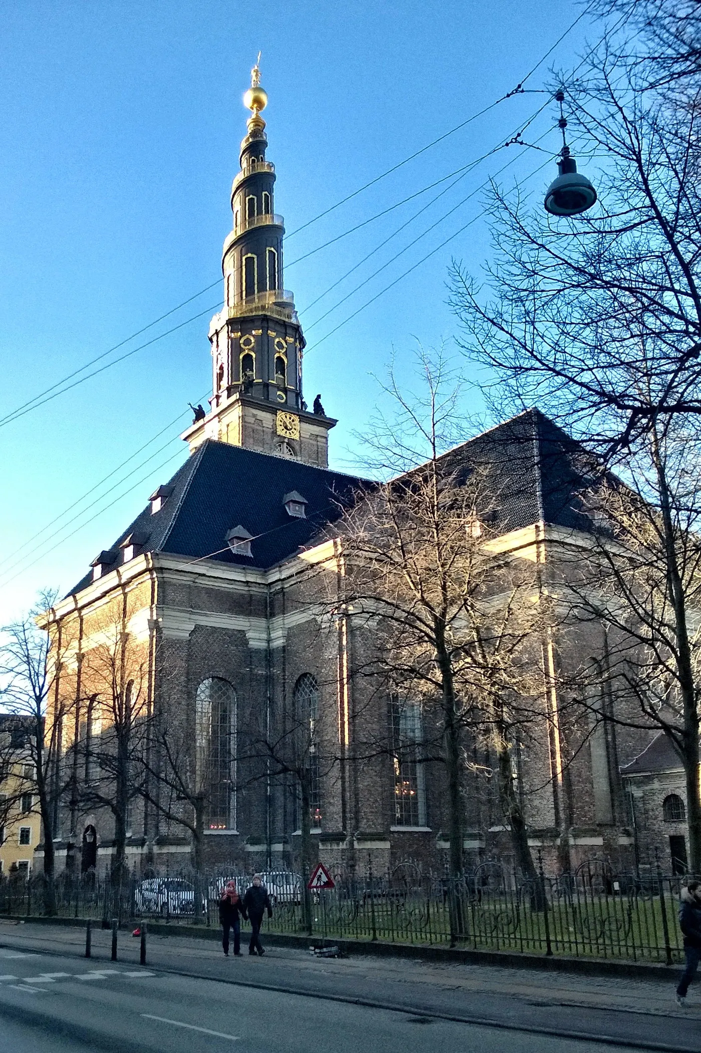 The Church of Our Saviour in Copenhagen from the street, a plain brick church under a black roof with a tall spire above it whose gilded staircase winds around the outside up to a golden globe