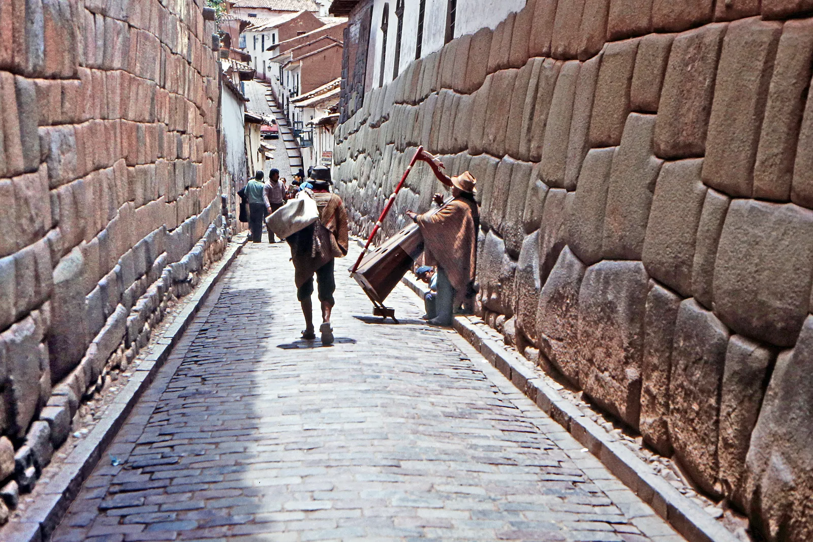 The cobbled pedestrian lane of Hatunrumiyoc in Cusco, running uphill between mortarless Inca walls on both sides with people walking along it