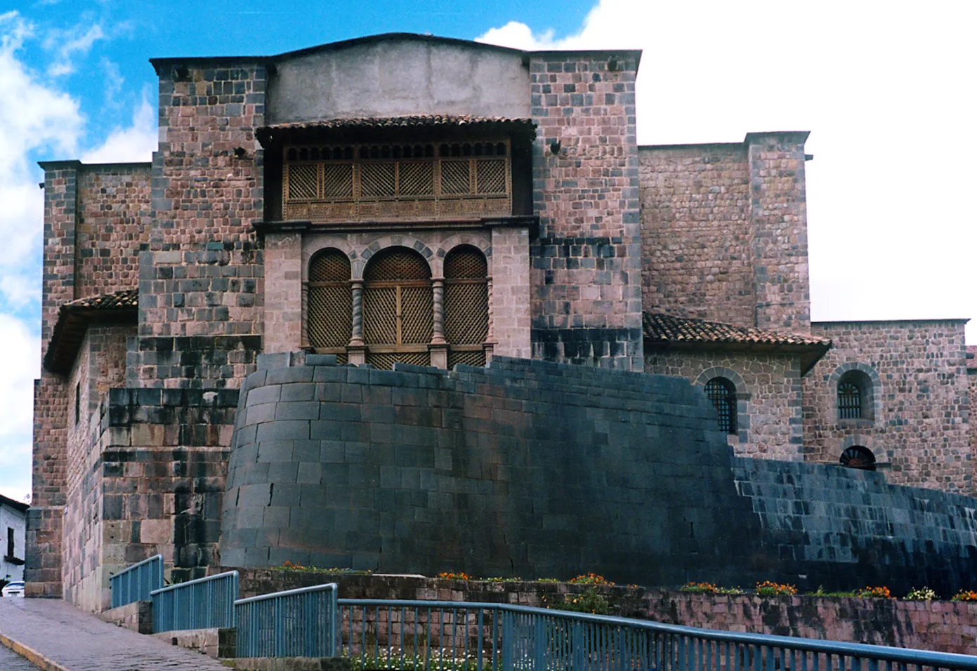 The convent of Santo Domingo in Cusco standing on the dark curved Inca wall of Qorikancha, with a colonial stone gallery and arched windows above the older stonework