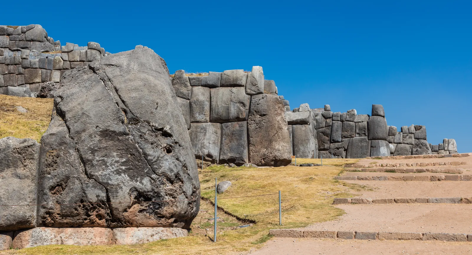The zigzag terrace wall at Sacsayhuamán above Cusco, built from limestone blocks taller than a person and fitted together without mortar, with a grass slope and stone steps in front