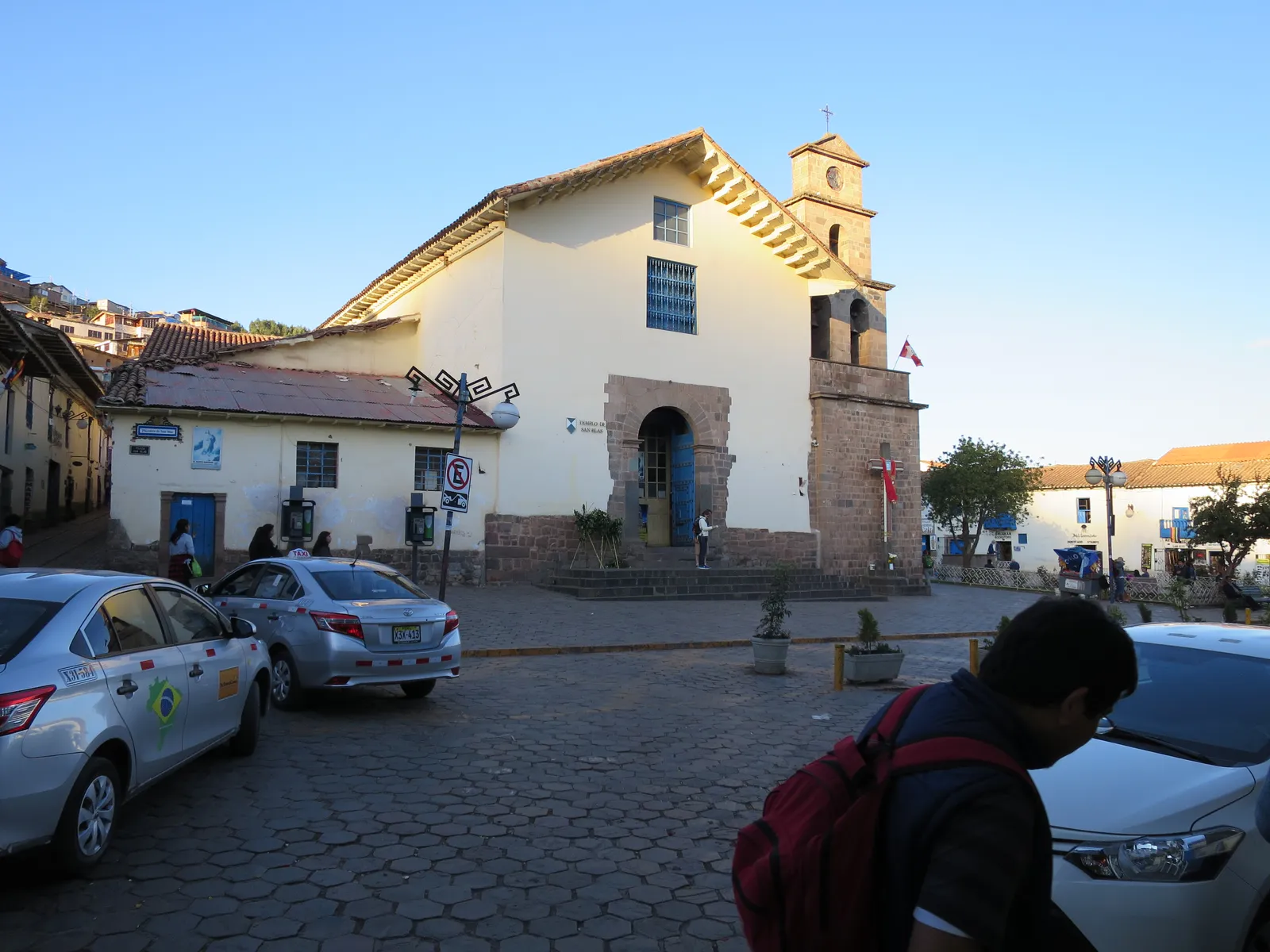 The whitewashed adobe church of San Blas in Cusco on its small cobbled plaza, with a single stone bell tower and the hillside houses of the quarter behind it