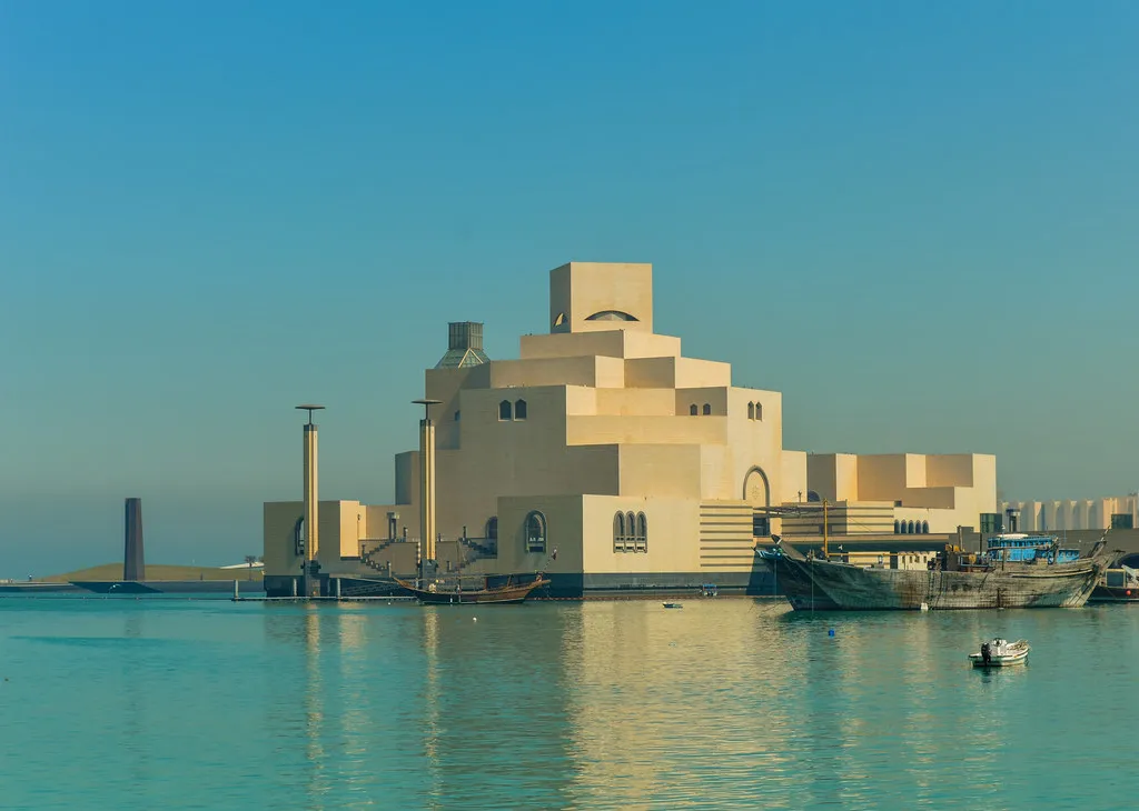 The Museum of Islamic Art in Doha across the water, its stacked cream limestone blocks stepping up to a tower, with dhows moored along the quay beside it