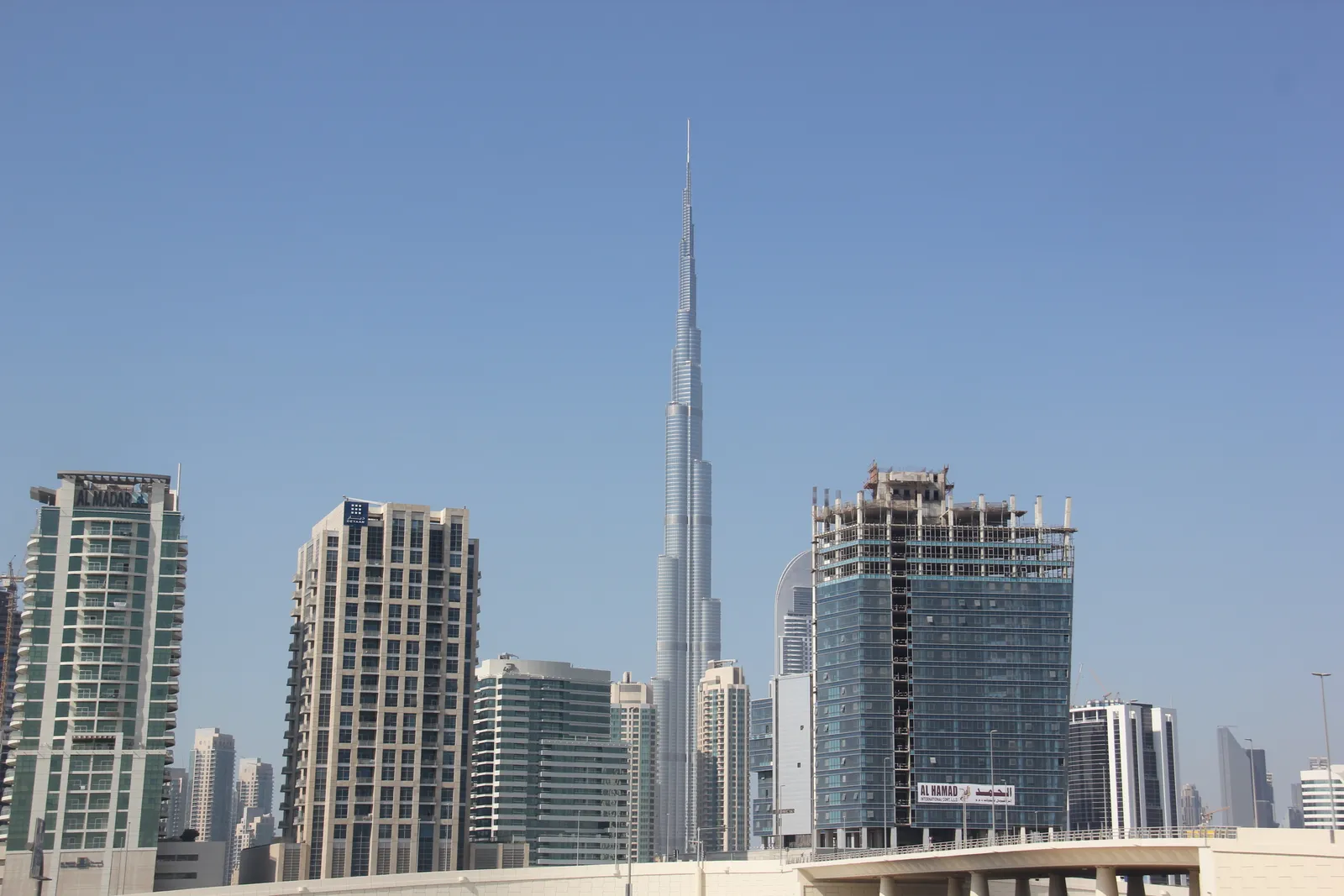 Burj Khalifa's stepped silver spire rising high above a row of mid-rise apartment towers in Downtown Dubai under a clear blue sky