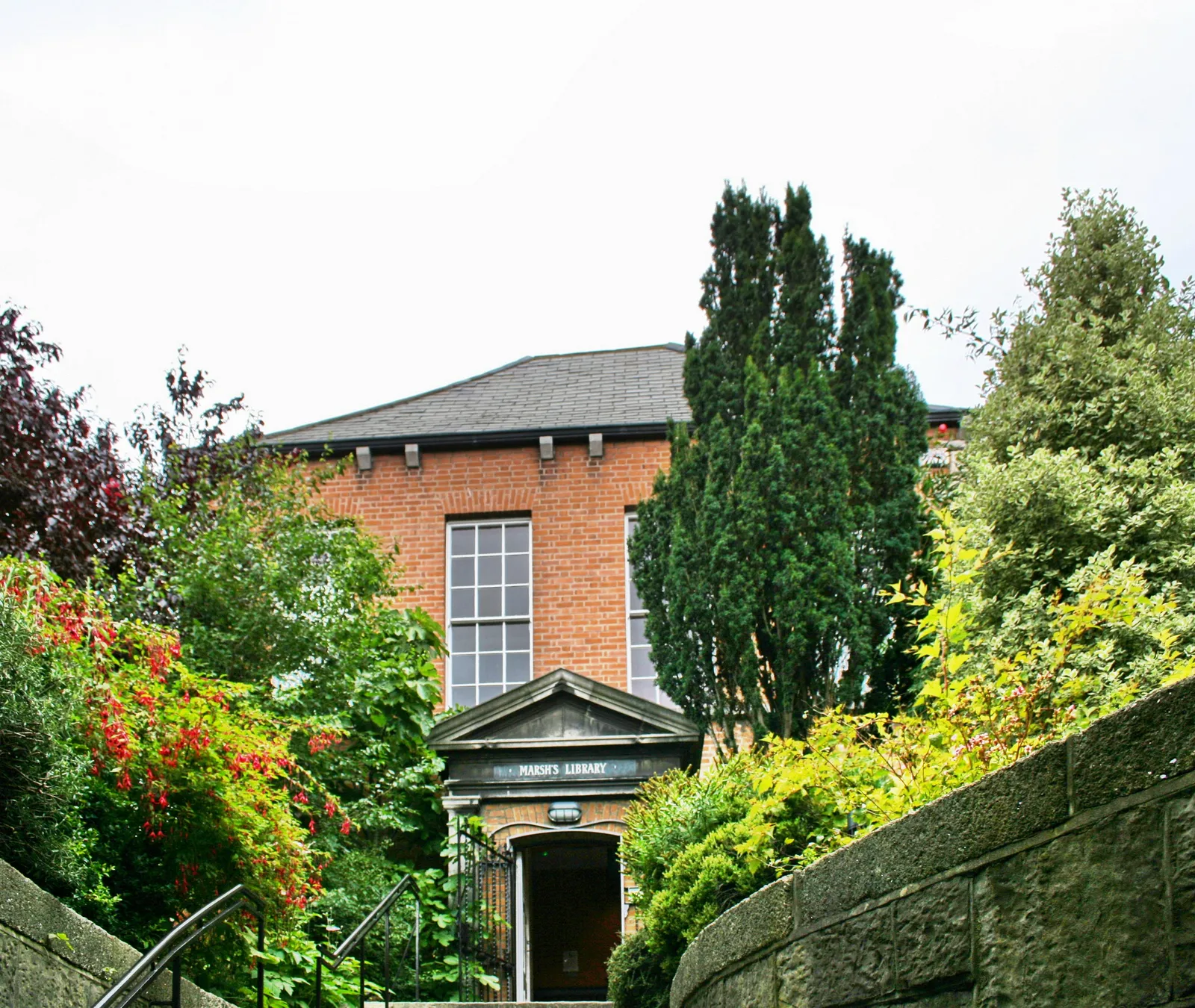 Marsh's Library in Dublin, a red-brick building with a small stone-pedimented doorway at the top of a flight of steps, half hidden behind hedges and trees