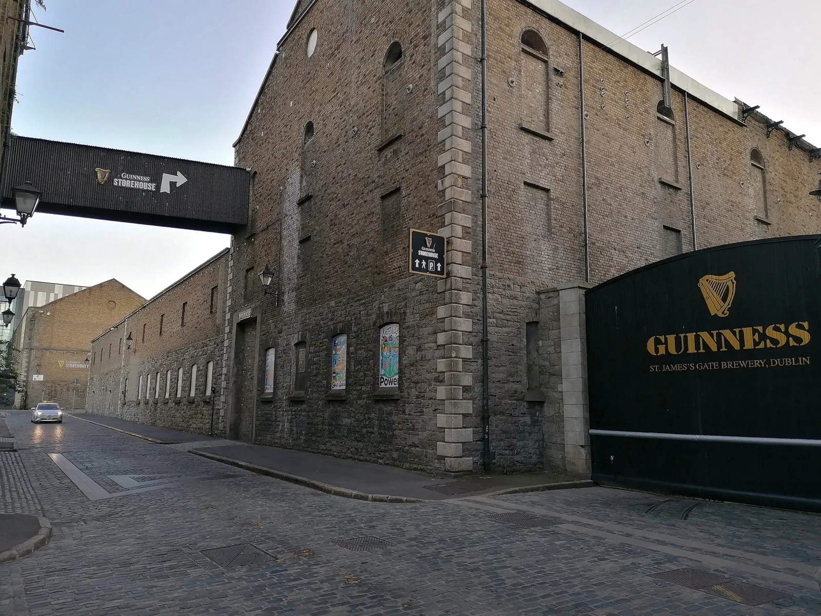 The black St James's Gate entrance to the Guinness brewery in Dublin, its gold harp and lettering set into the wall beside the tall stone brewery buildings on a cobbled street