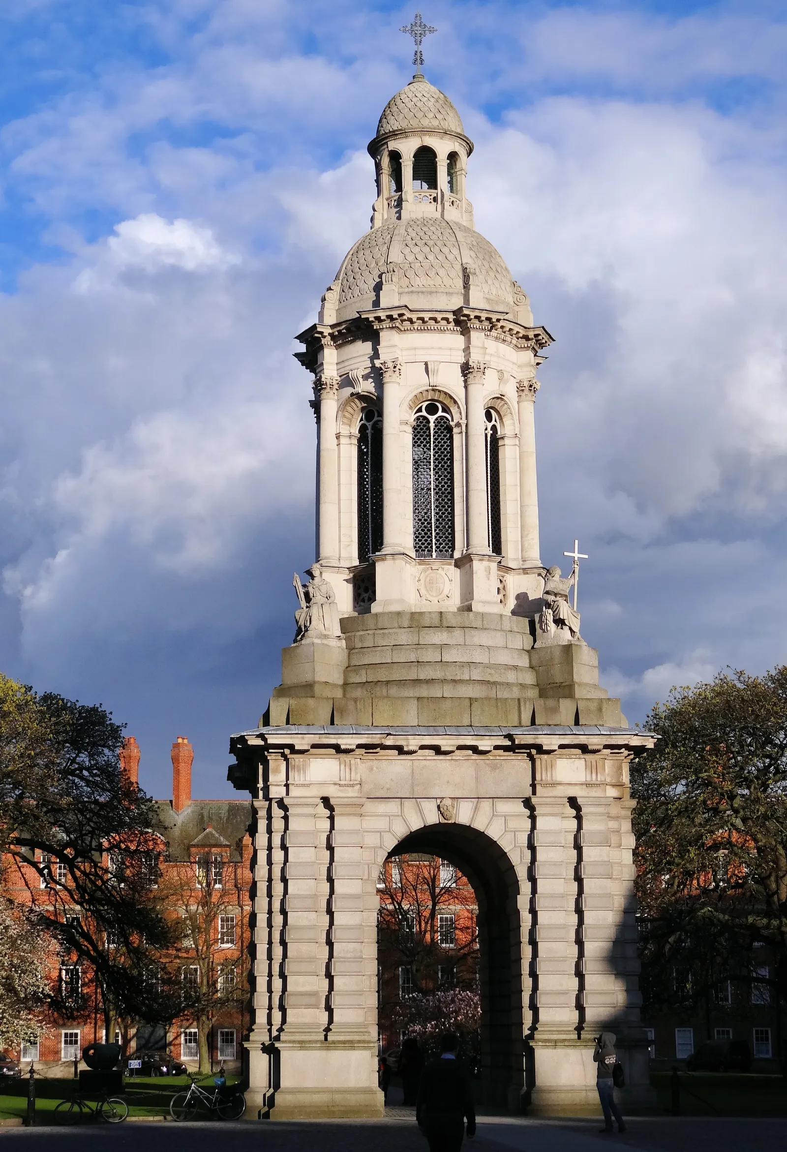 The Campanile at Trinity College Dublin, a tall stone bell tower on an arched base standing in the middle of the cobbled square, with the red-brick Rubrics building and bare trees behind it