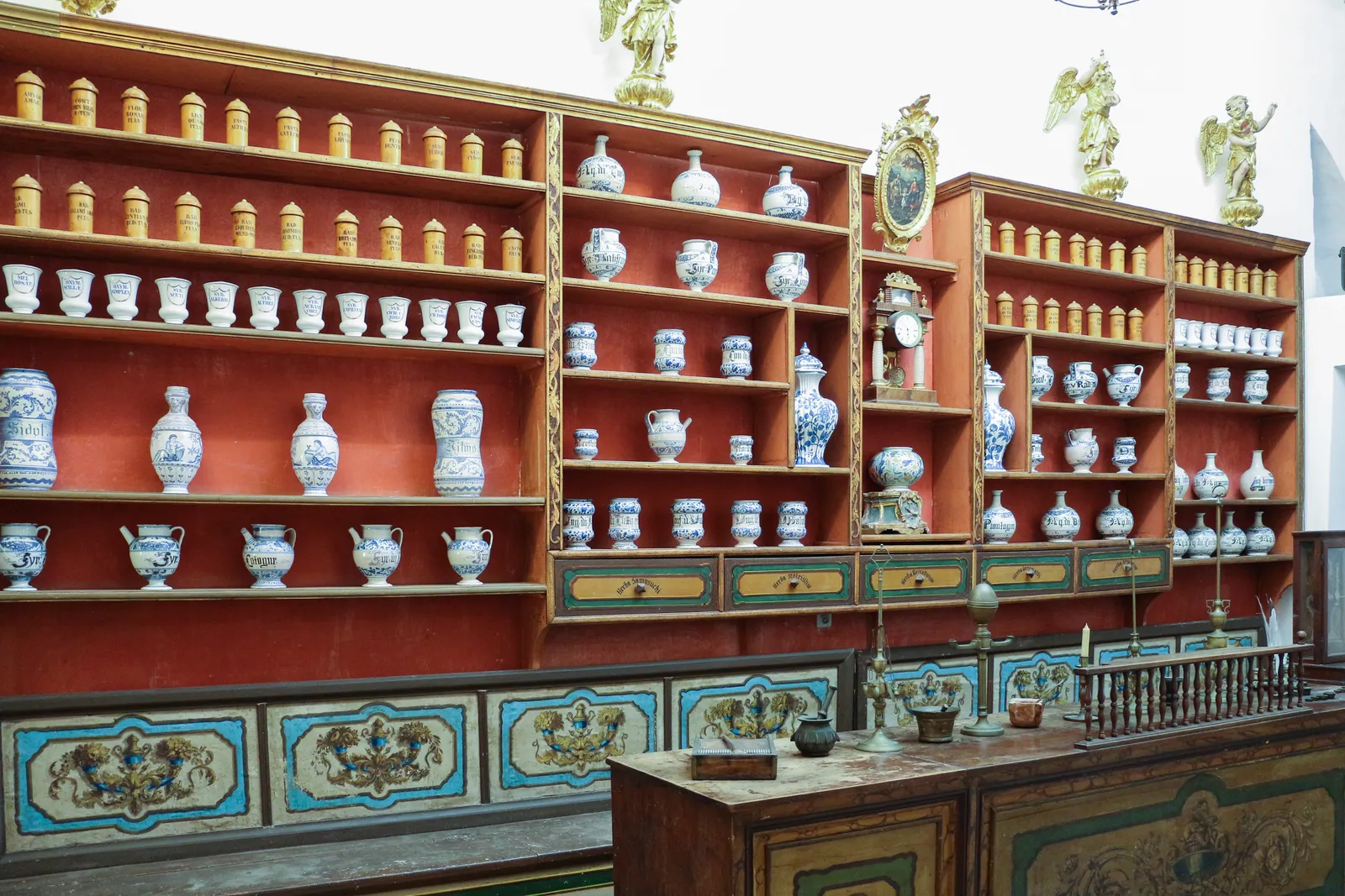 The old pharmacy inside Dubrovnik's Franciscan monastery, rows of blue and white ceramic apothecary jars on deep red shelves above a painted wooden counter