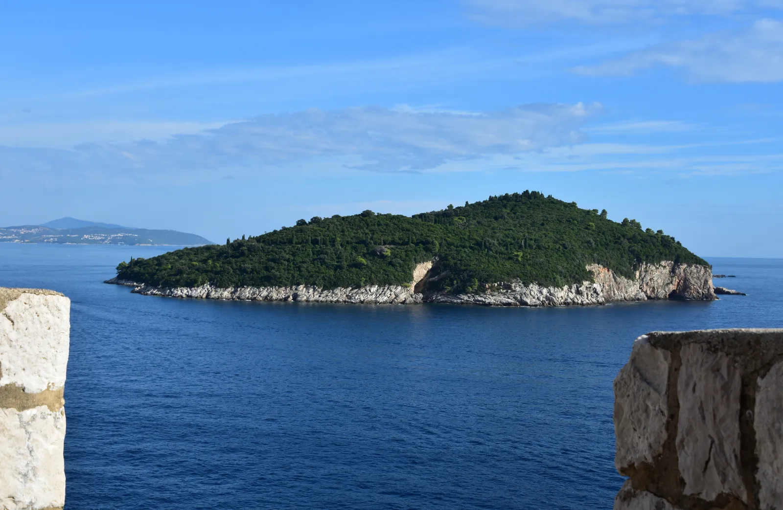 Lokrum, a low wooded island ringed by pale rock, sitting in dark blue water a short way off Dubrovnik, framed between two blocks of the city wall