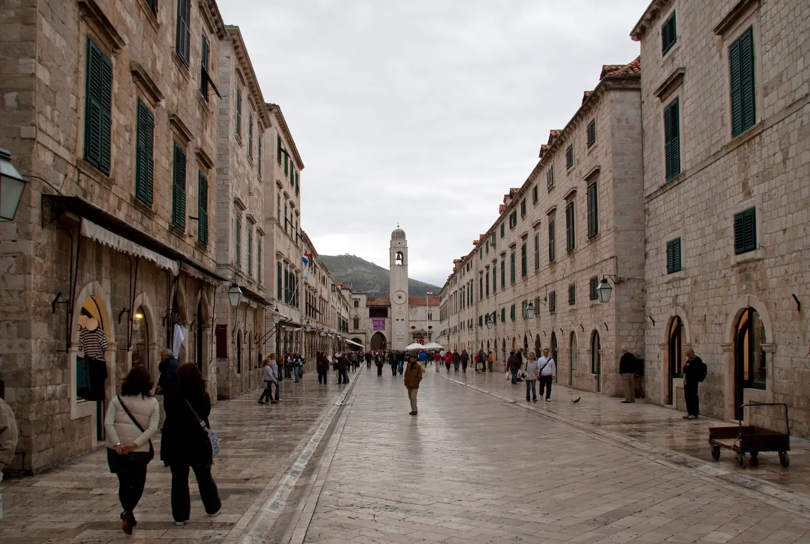 Stradun in Dubrovnik seen along its length, a broad limestone street polished to a shine between matching stone houses, with the bell tower at the far end and people walking down the middle