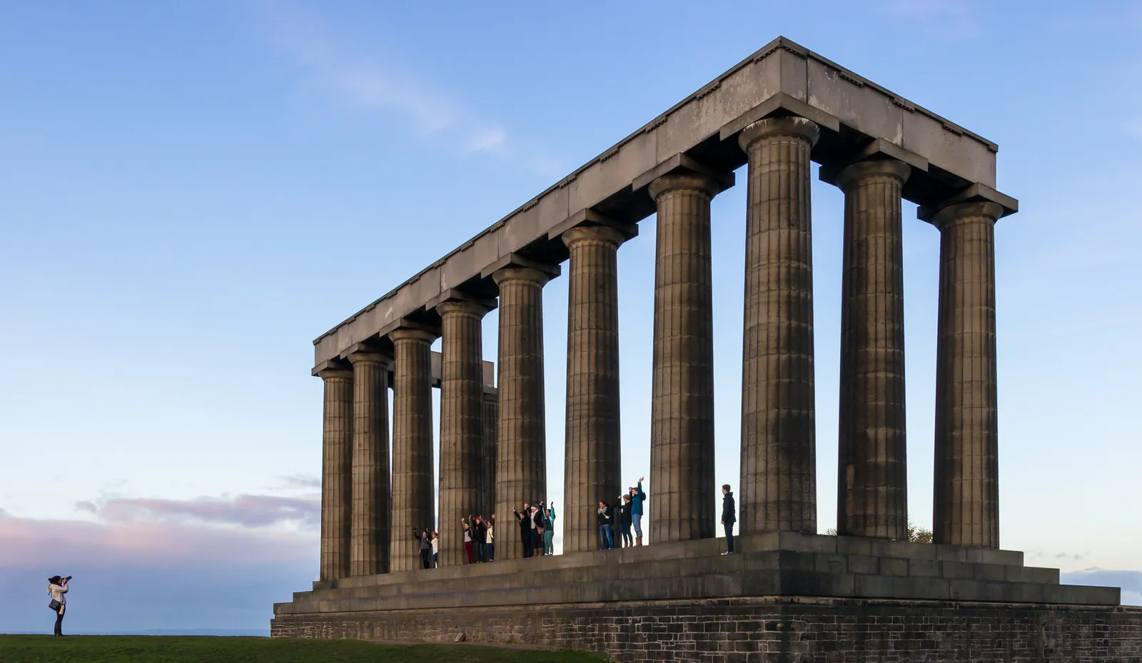 The National Monument on Calton Hill in Edinburgh, twelve tall Doric columns carrying a section of architrave on a stepped stone platform, with visitors standing between them for scale