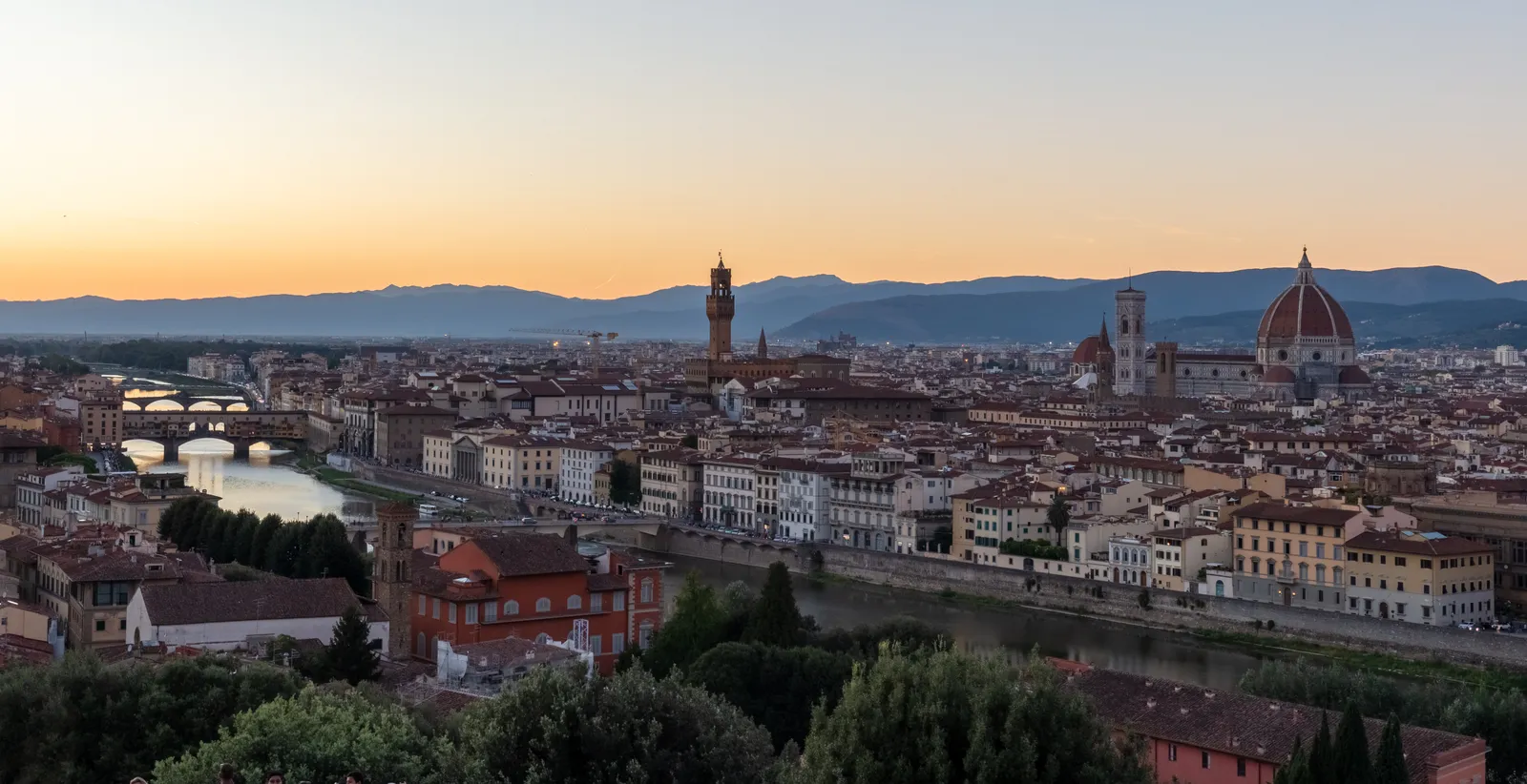 Sunset skyline of Florence with the Duomo, Palazzo Vecchio, and Ponte Vecchio visible along the Arno river