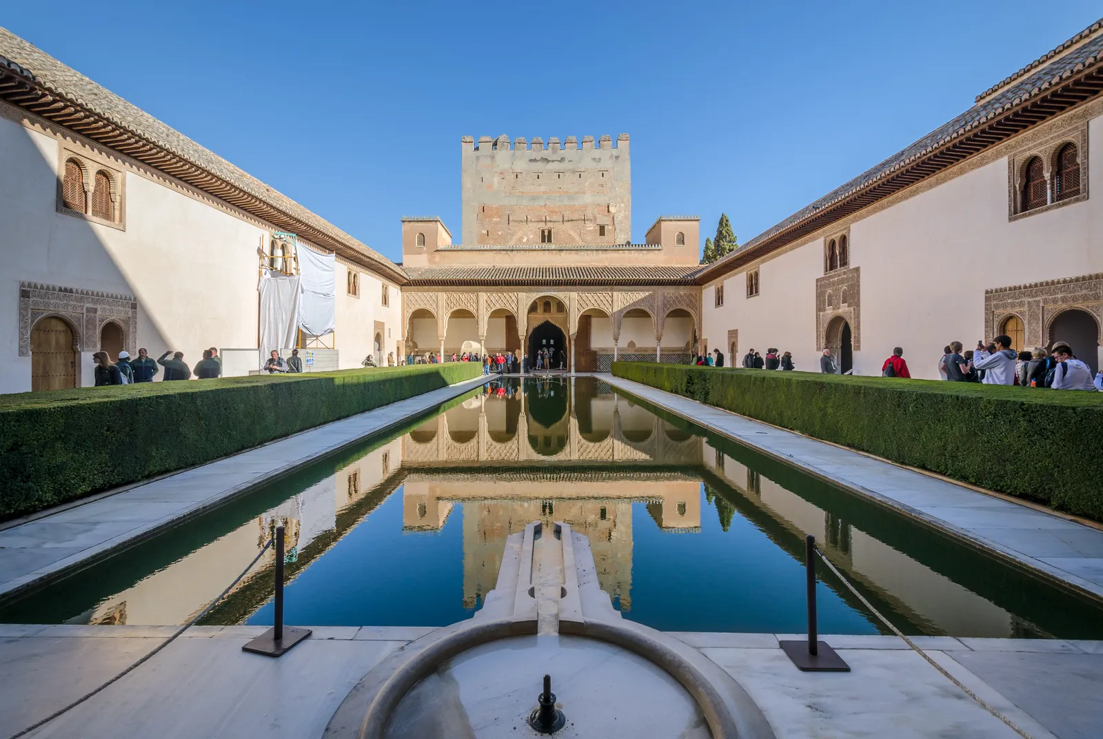 The Court of the Myrtles in the Alhambra, a long rectangular pool between clipped myrtle hedges with the crenellated Comares Tower reflected in the water at the far end