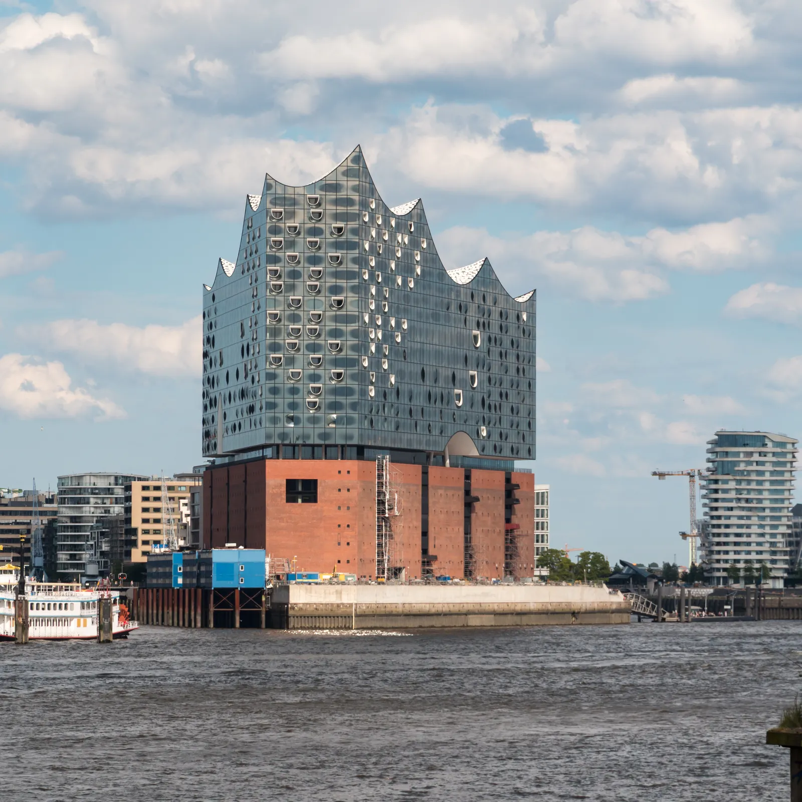The Elbphilharmonie in Hamburg seen from across the Elbe, its wave-shaped glass upper half sitting directly on the square red-brick warehouse that forms its base
