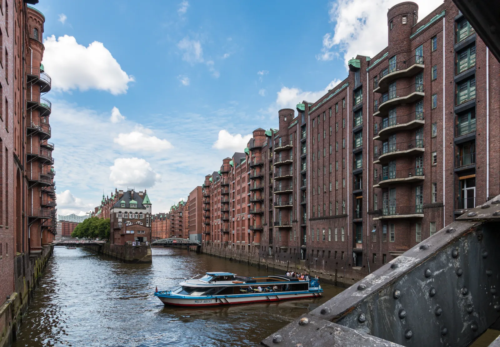 A canal running between rows of red-brick Speicherstadt warehouses in Hamburg, with a tour boat below and the turreted Wasserschloss building at the far end