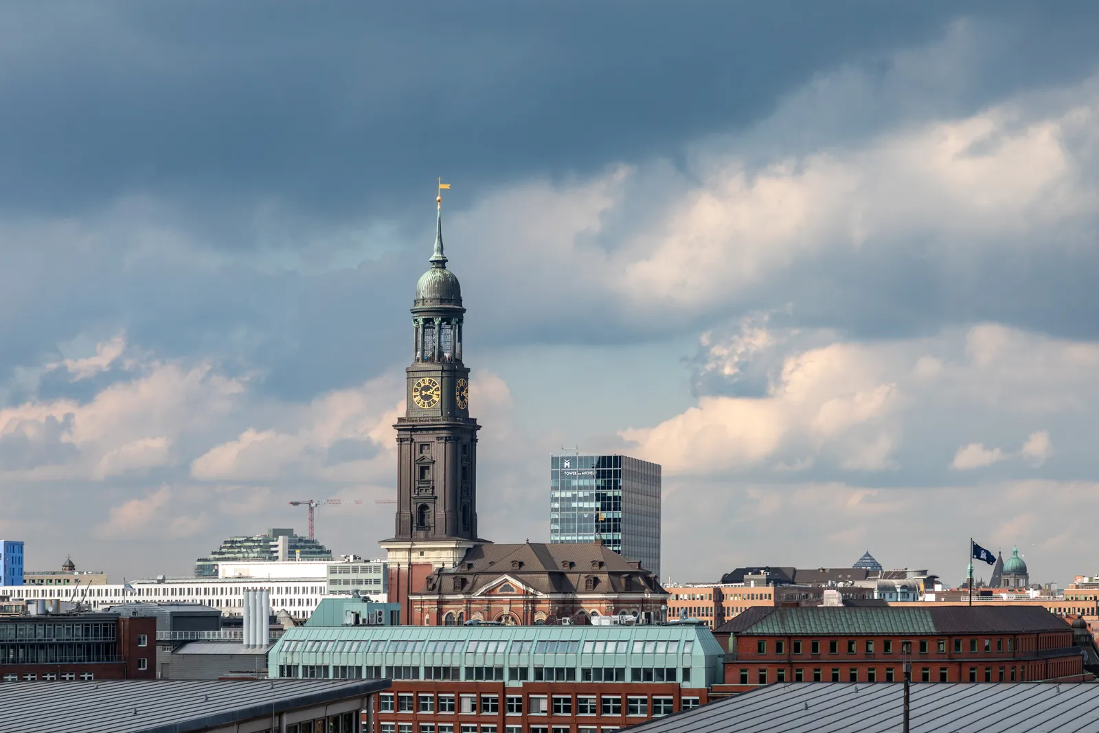 The copper-green tower and clock face of St. Michael's Church in Hamburg rising above the surrounding rooftops under a cloudy sky