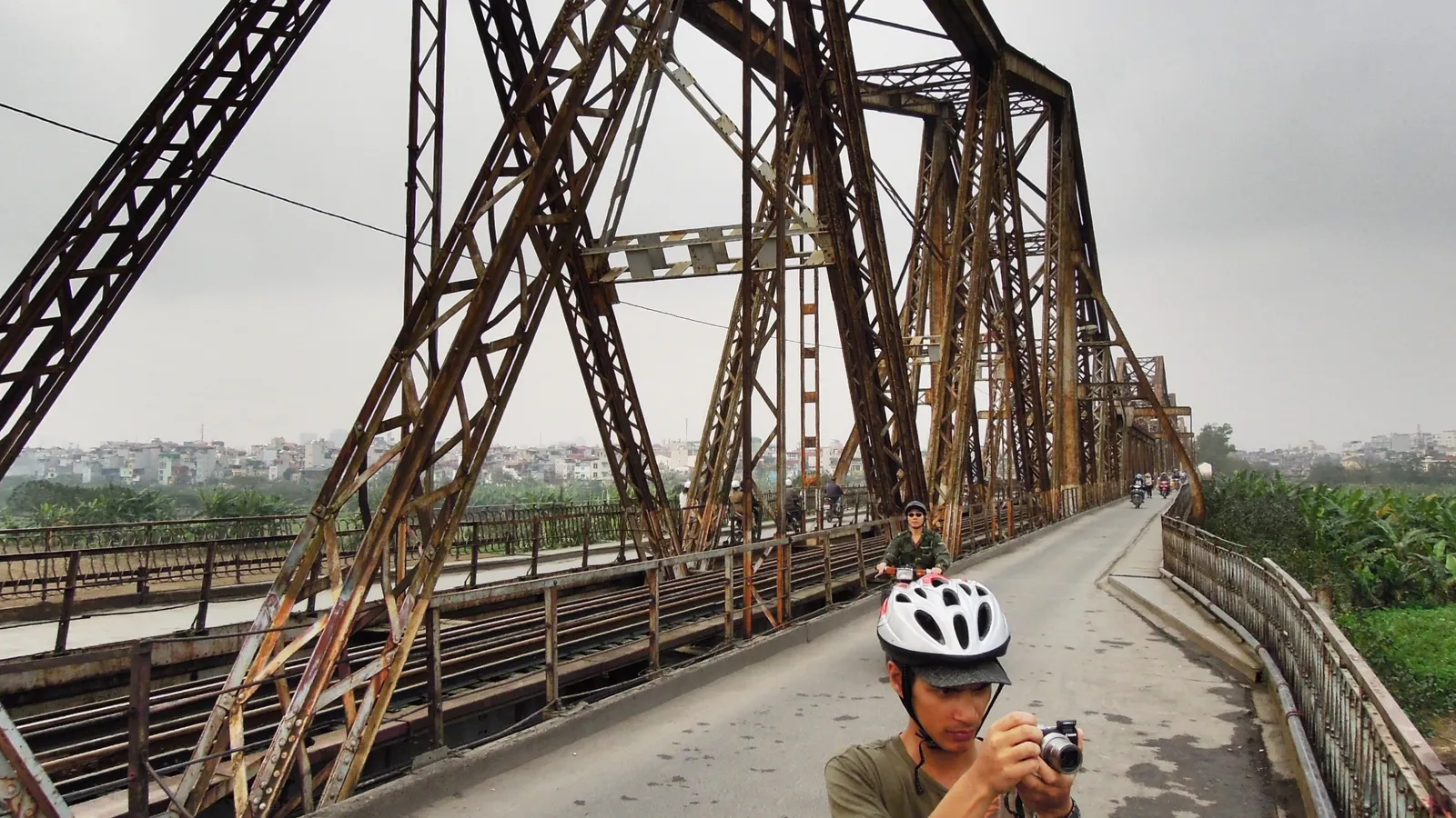 The deck of Long Bien Bridge in Hanoi between its riveted steel trusses, with a narrow roadway, a raised footway to one side and the rail track running along the middle