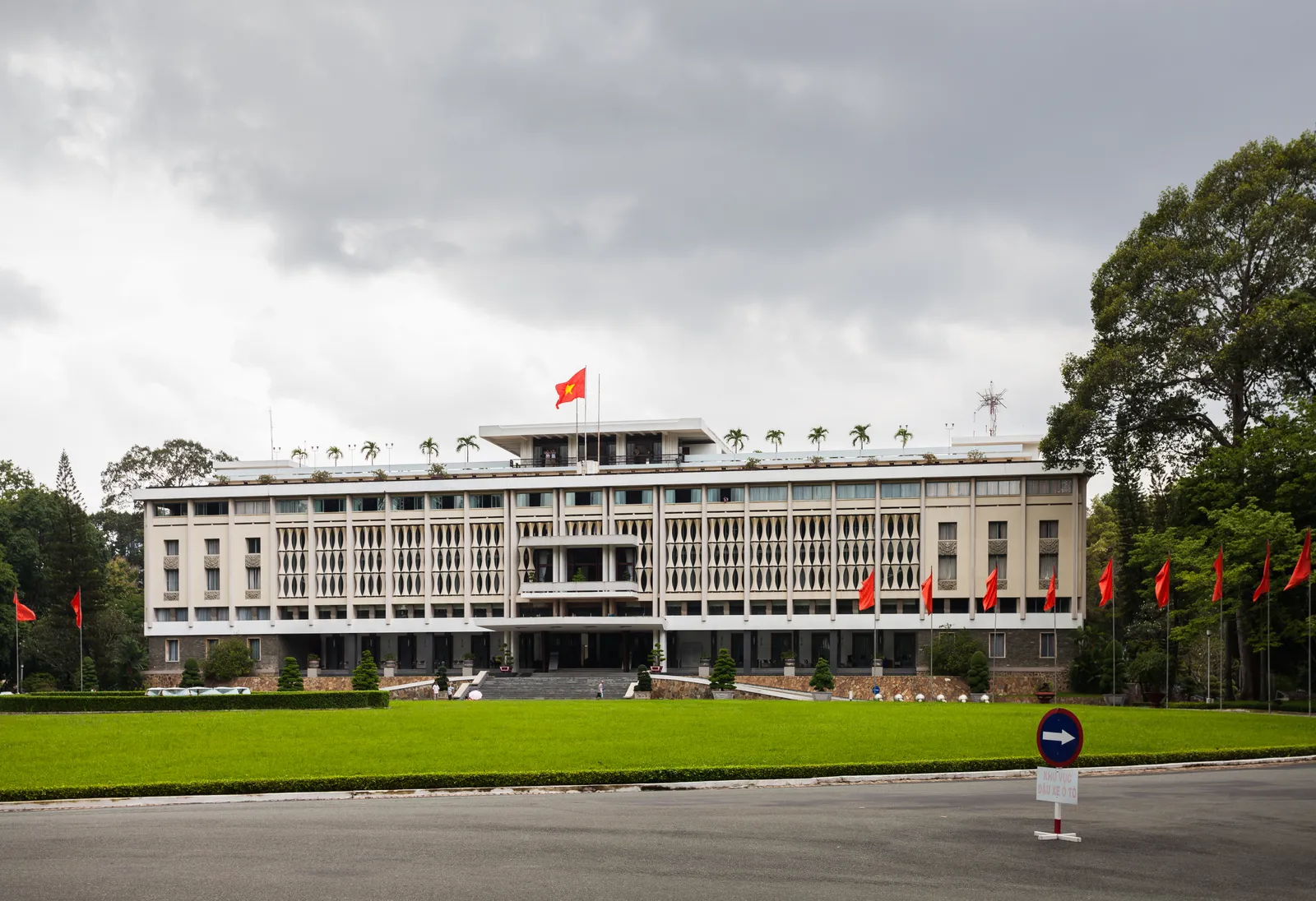 The long white modernist frontage of Independence Palace in Ho Chi Minh City behind its lawn, a red Vietnamese flag flying from the roof and a row of flags along the forecourt