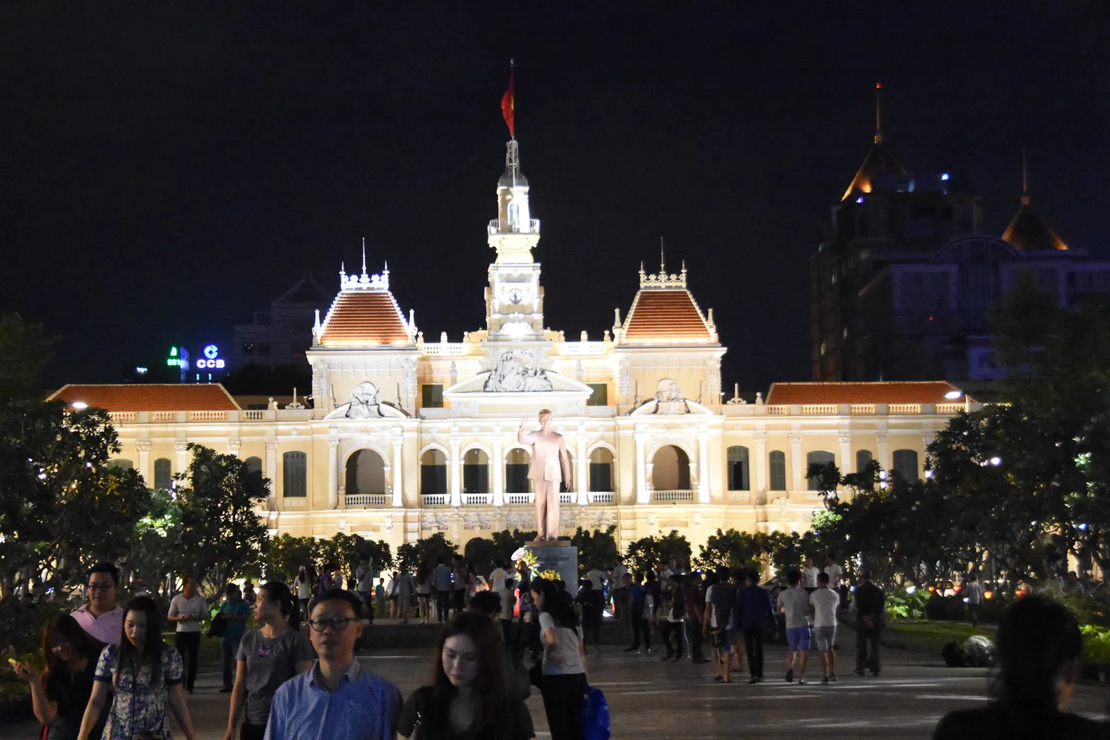Ho Chi Minh City's People's Committee building floodlit at night at the head of the Nguyen Hue promenade, its cream French colonial facade and central clock tower above a crowd filling the paved strip