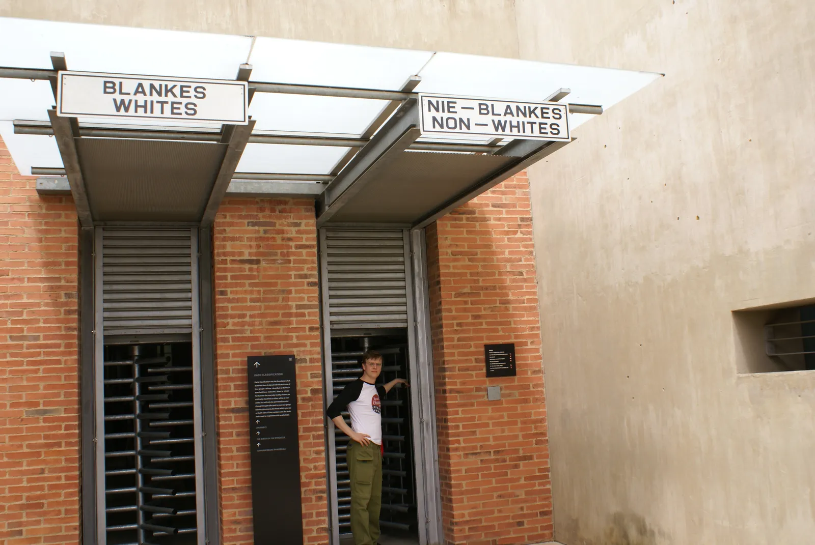 The two entrances at the Apartheid Museum in Johannesburg, steel turnstiles in a red brick wall under signs reading BLANKES WHITES and NIE-BLANKES NON-WHITES