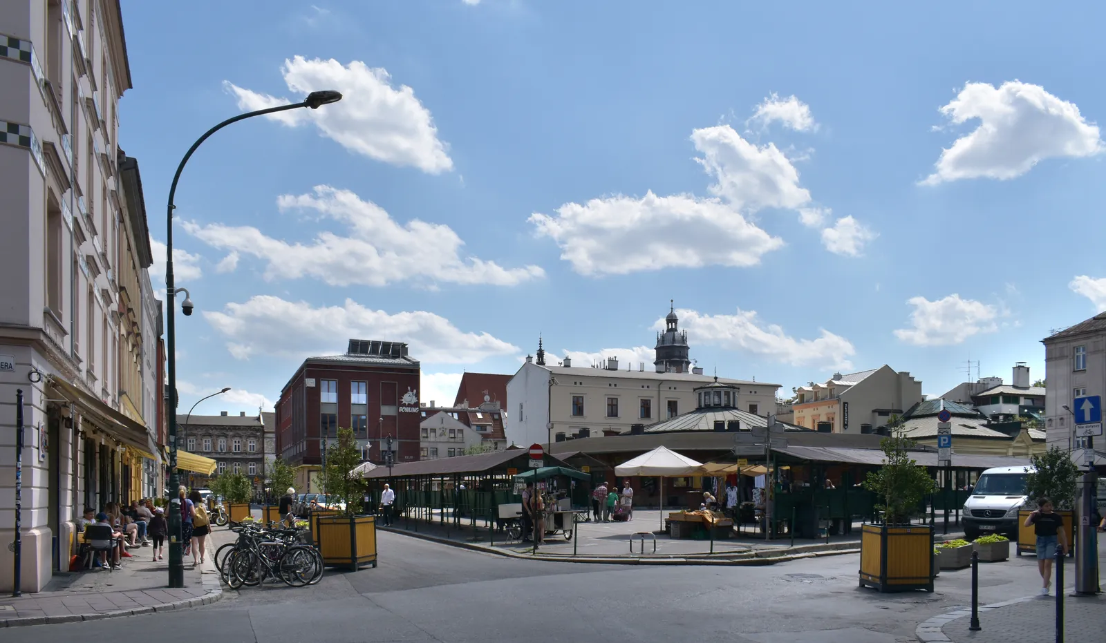 Plac Nowy in Kraków's Kazimierz district, a low round brick market hall standing alone in the middle of an open square, ringed by green food stalls and surrounded by tenement buildings