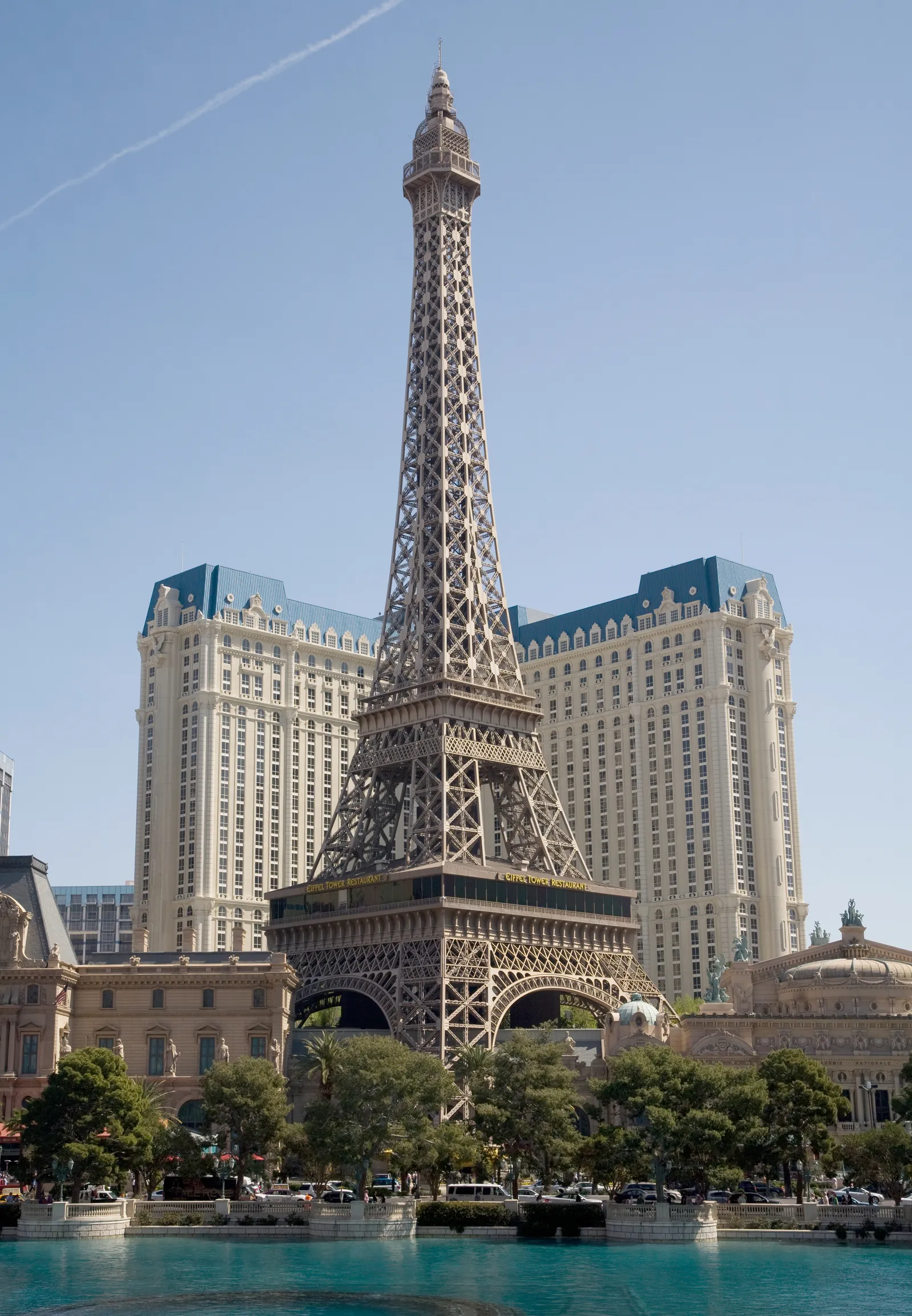 The half-scale Eiffel Tower replica at Paris Las Vegas rising out of the resort's blue-roofed facade, photographed by day across the Bellagio's lake